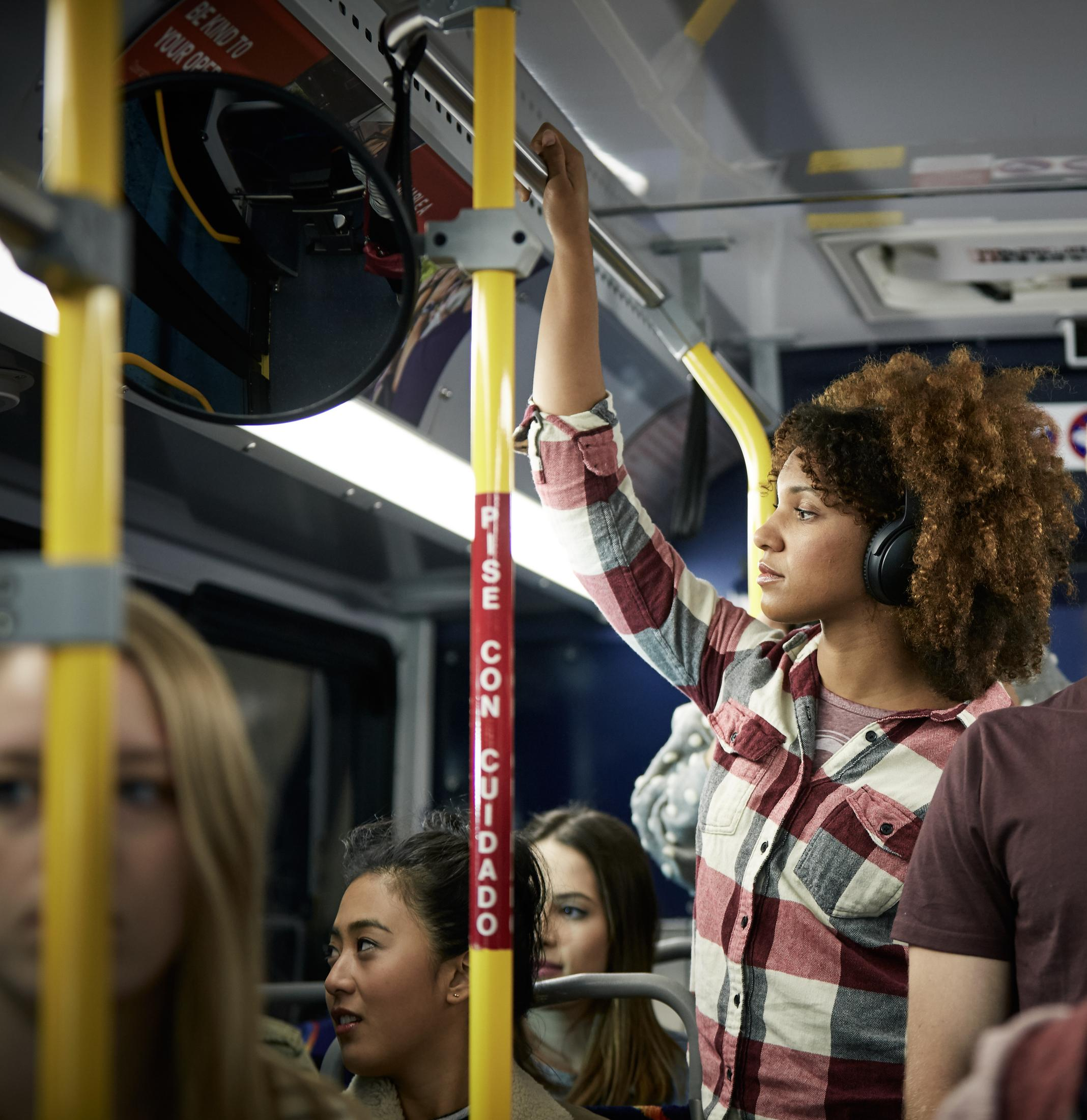 Eine Frau in einem Bus mit Kopfhörern, die sich an einer Stange festhält.