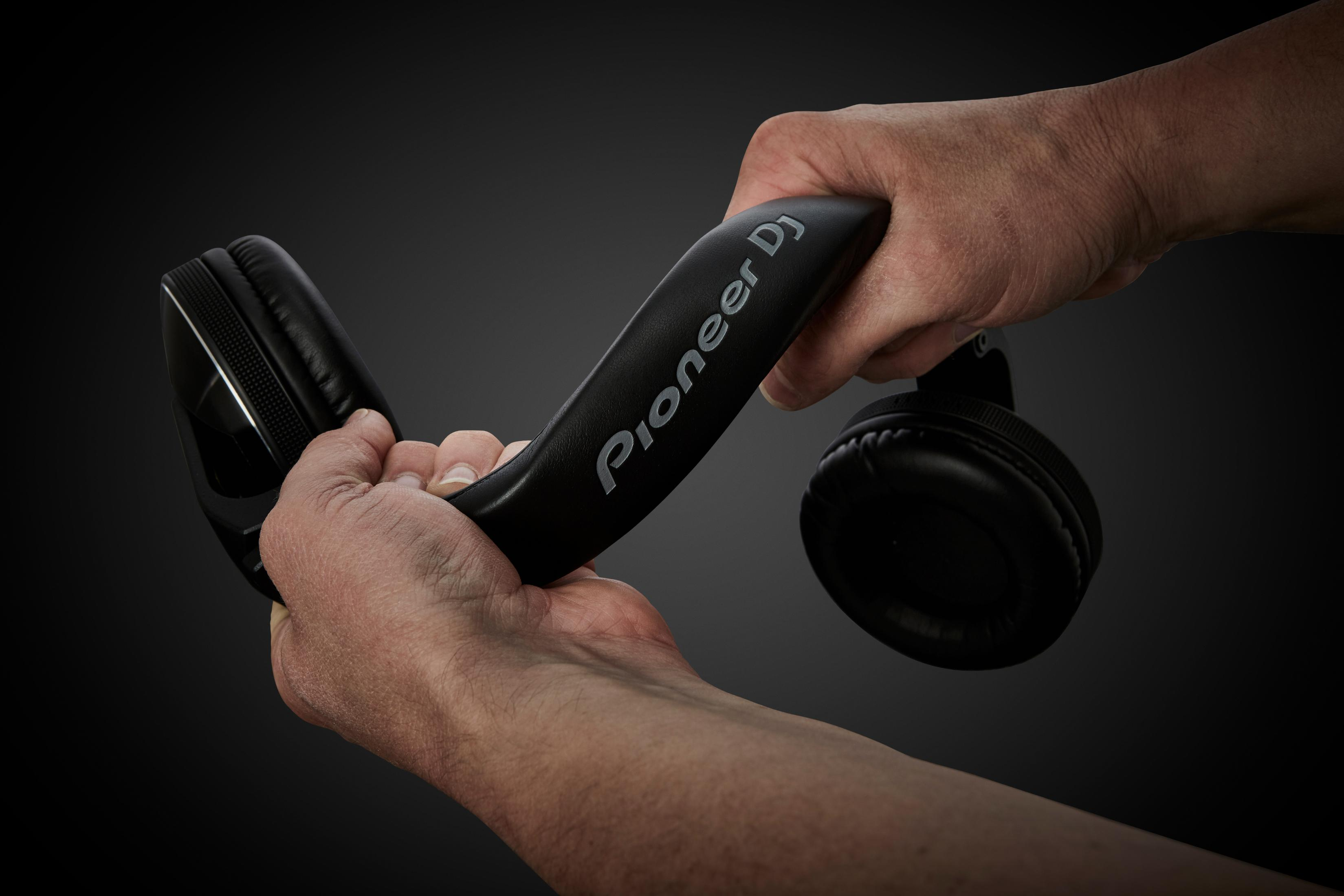 Dłonie trzymające i wyginające czarne słuchawki Pioneer DJ na ciemnym tle.