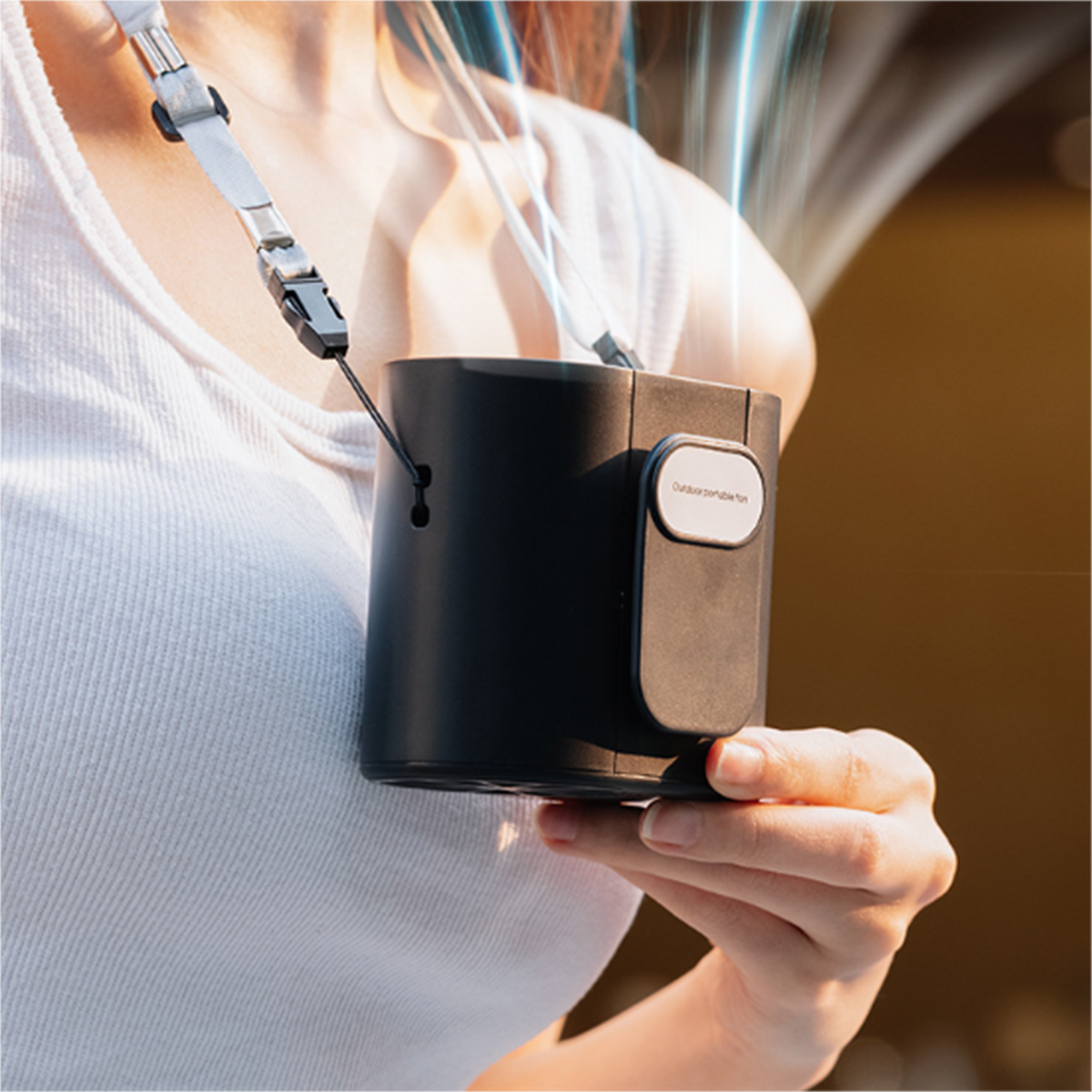 Eine Person hält einen schwarzen tragbaren Ventilator mit Gurt, im Freien.