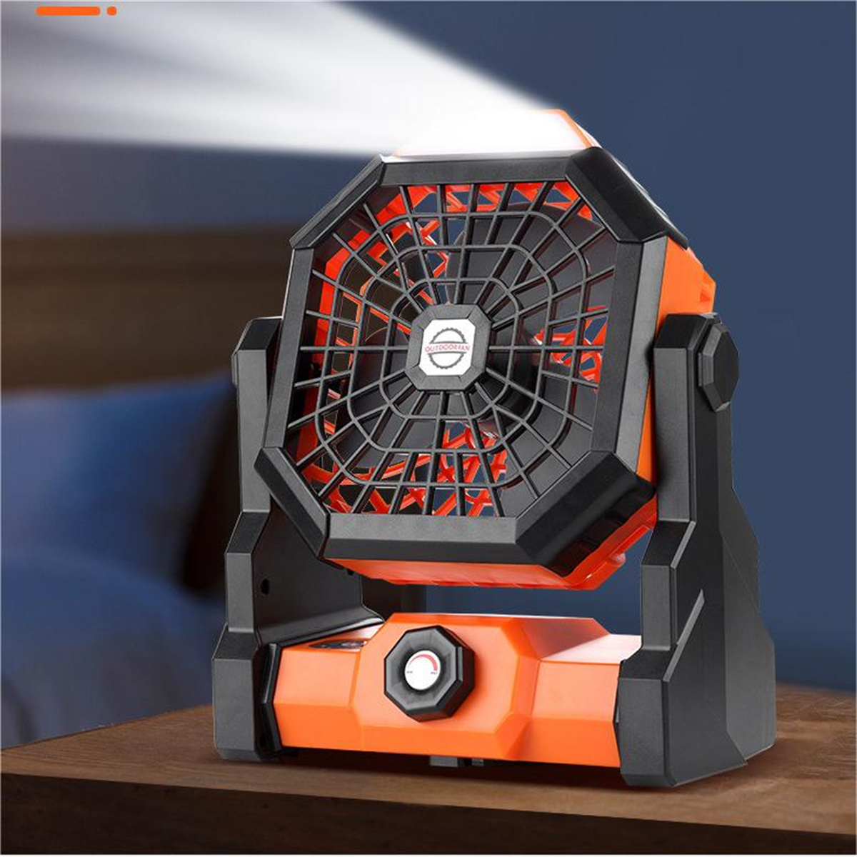Ein orangefarbener und schwarzer Ventilator steht auf einer Holzoberfläche, ist nach oben abgewinkelt und wird von einer Lichtquelle beleuchtet.