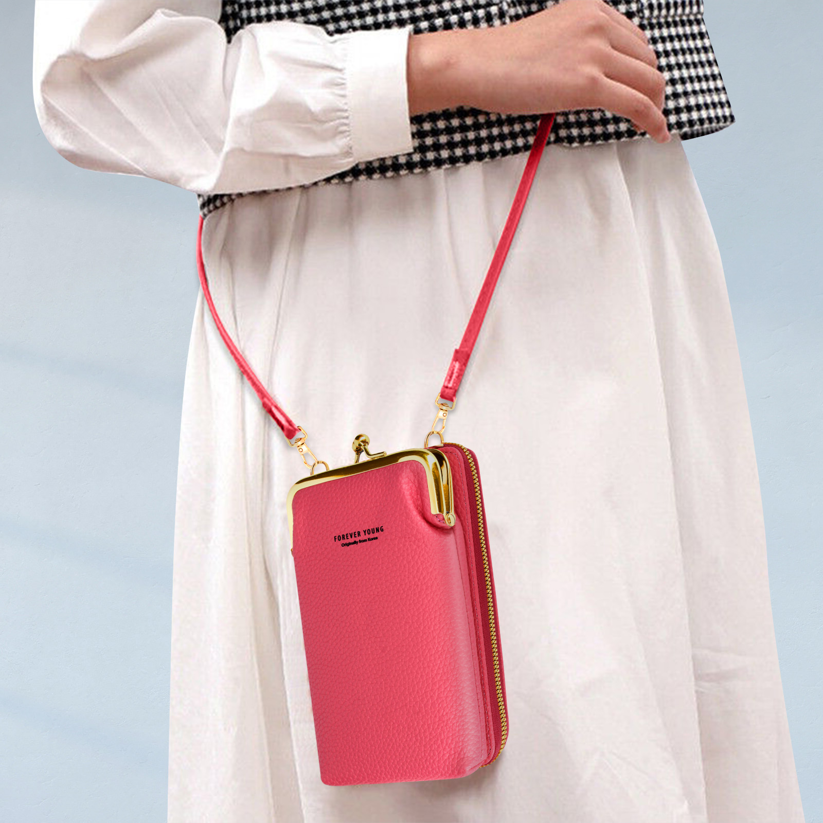 Une femme tient un sac à main rose rectangulaire avec un fermoir doré et une sangle rouge. Le sac est fermé.