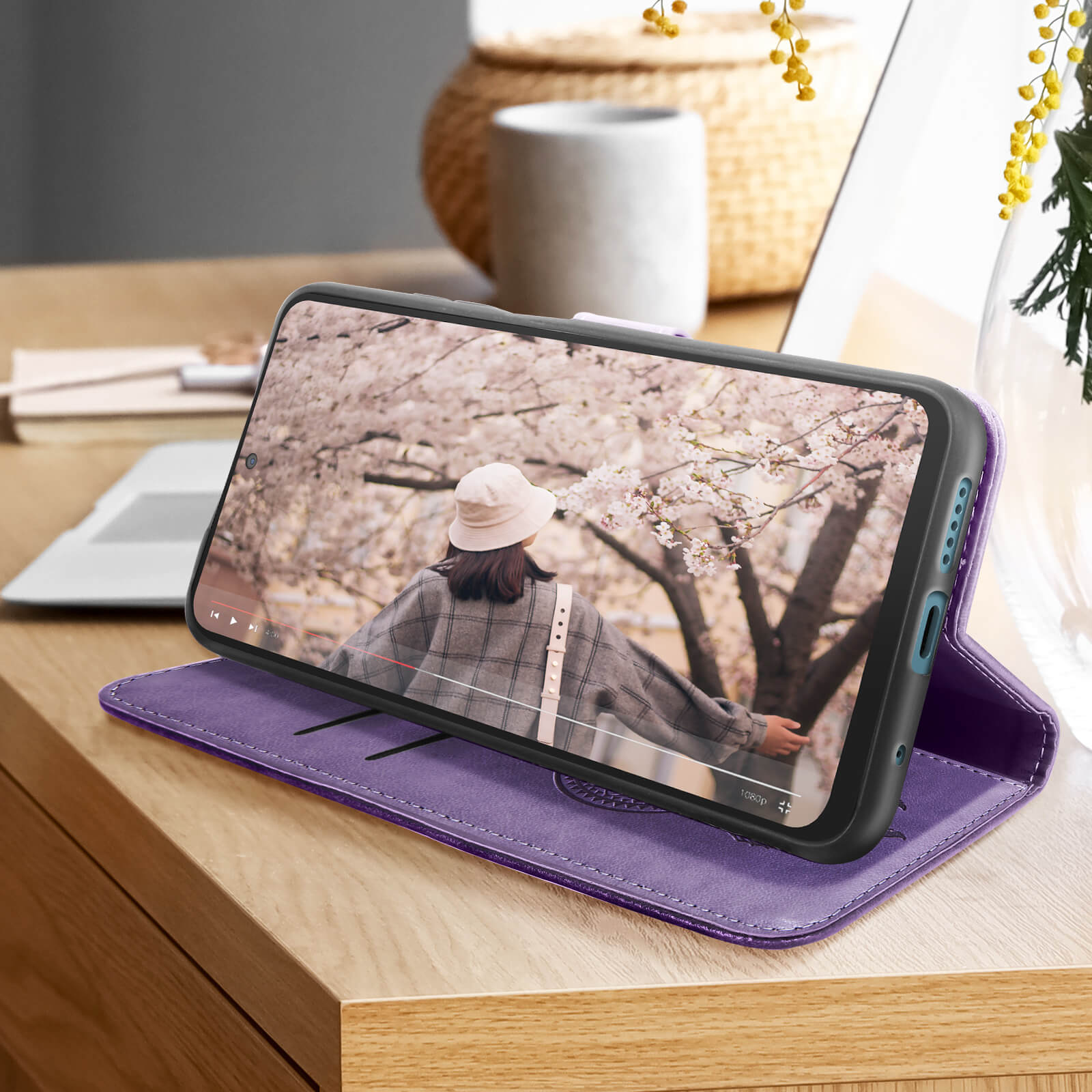 Telefono in custodia viola che mostra video di una donna, su superficie di legno.