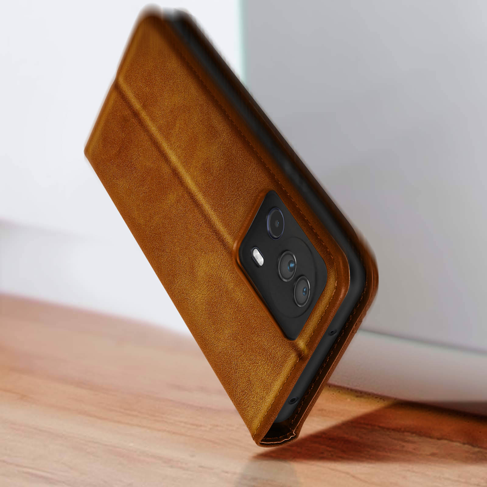 Custodia marrone per telefono, vista angolata, su superficie in legno. Tre lenti della fotocamera.