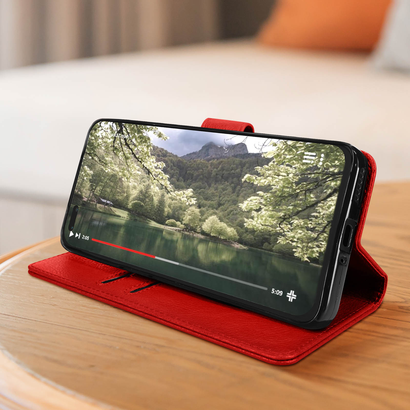 Ein Smartphone, das ein Video auf einer roten Lederhülle anzeigt, auf einem Holztisch platziert.