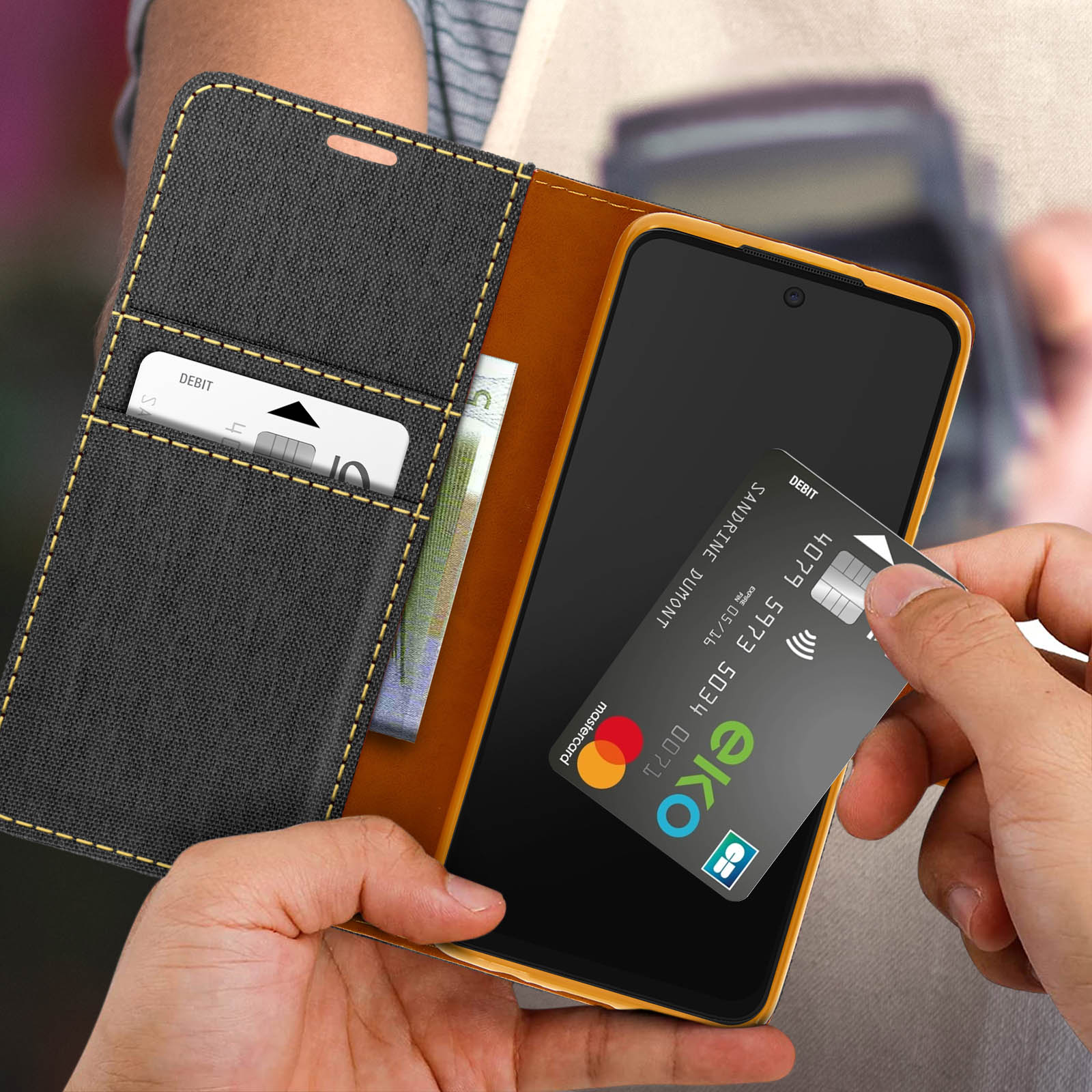 Un telefono nero in una custodia aperta, una carta di credito viene tenuta alzata. Sfondo sfocato.