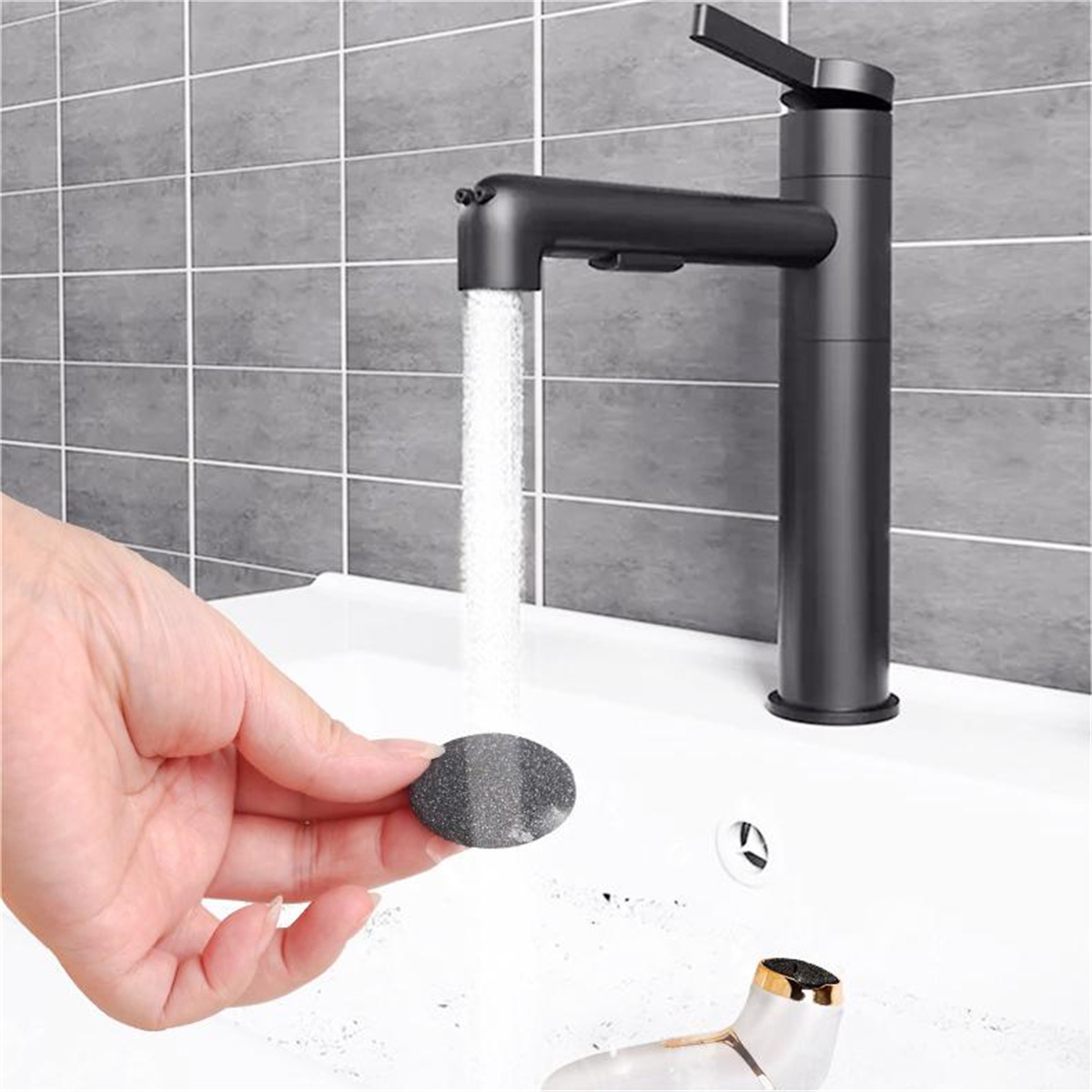 Eine Hand hält einen grauen Stein unter einem mattschwarzen Wasserhahn mit fließendem Wasser und einem weißen Waschbecken.