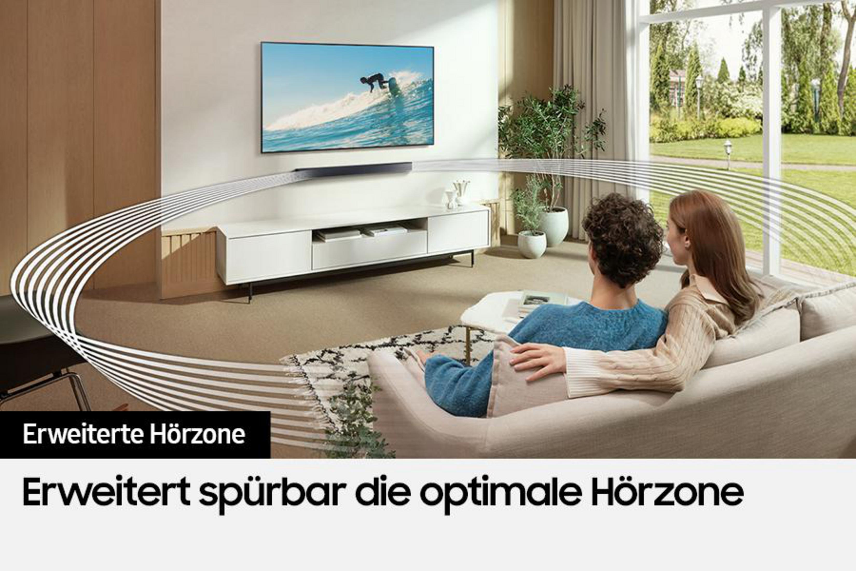 Para na sofie ogląda telewizję, z soundbarem i dużym ekranem na ścianie.