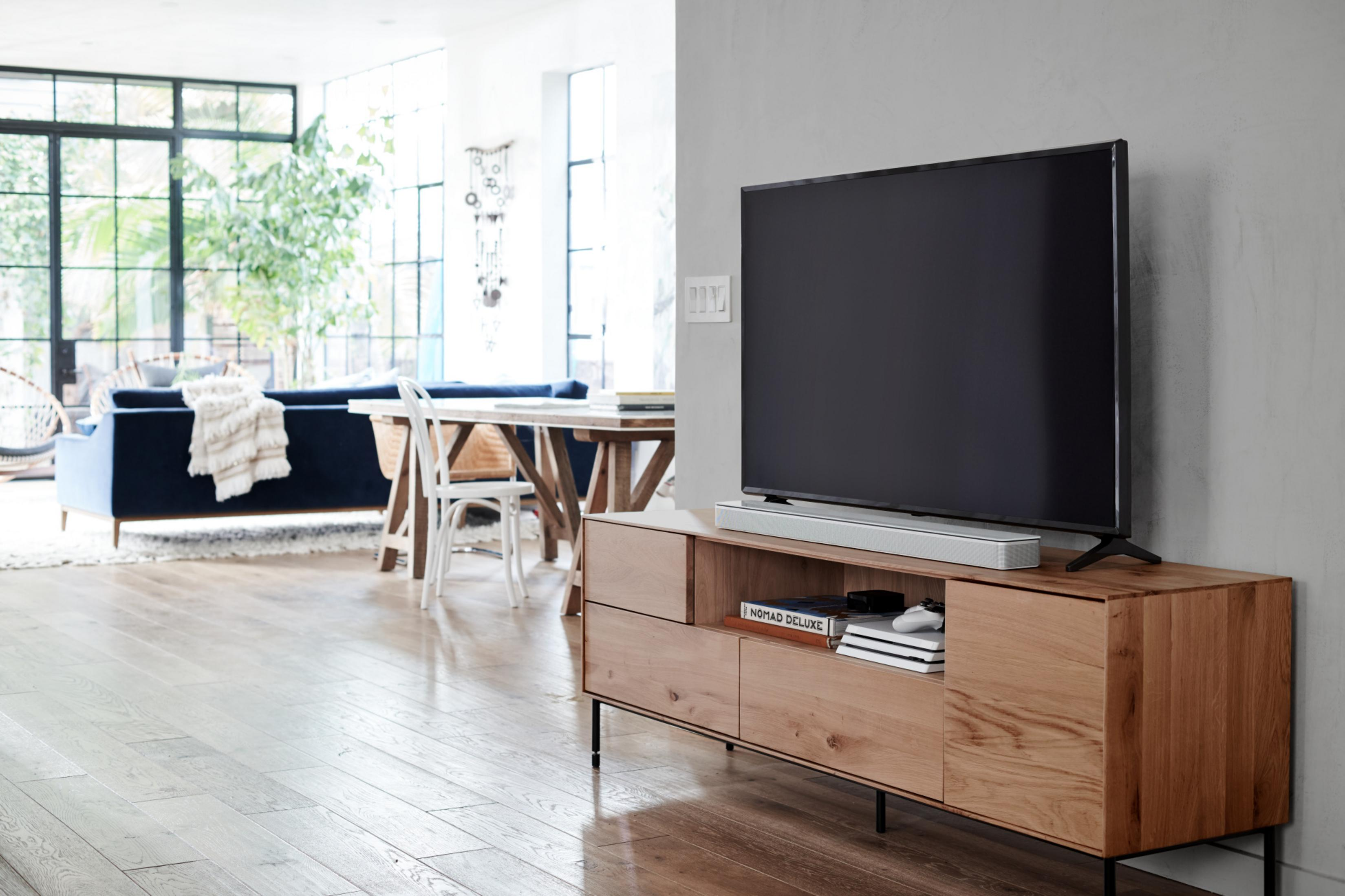 Wohnzimmer mit großem TV auf einem Holzschrank. Blaues Sofa, weißer Stuhl, Holztisch und Boden.