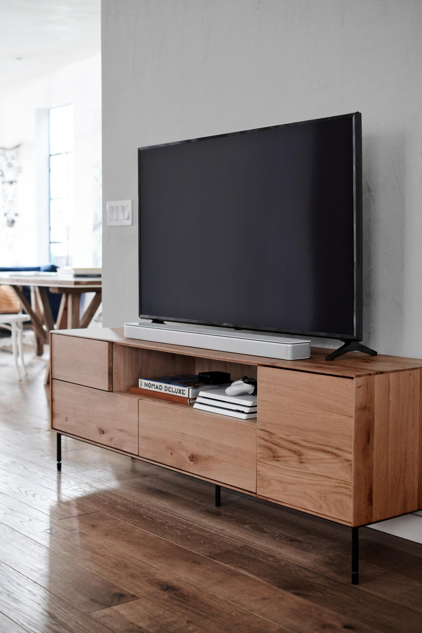 Wohnzimmer mit Fernseher auf Holzständer, Soundbar, Büchern und Konsole. Holzboden.