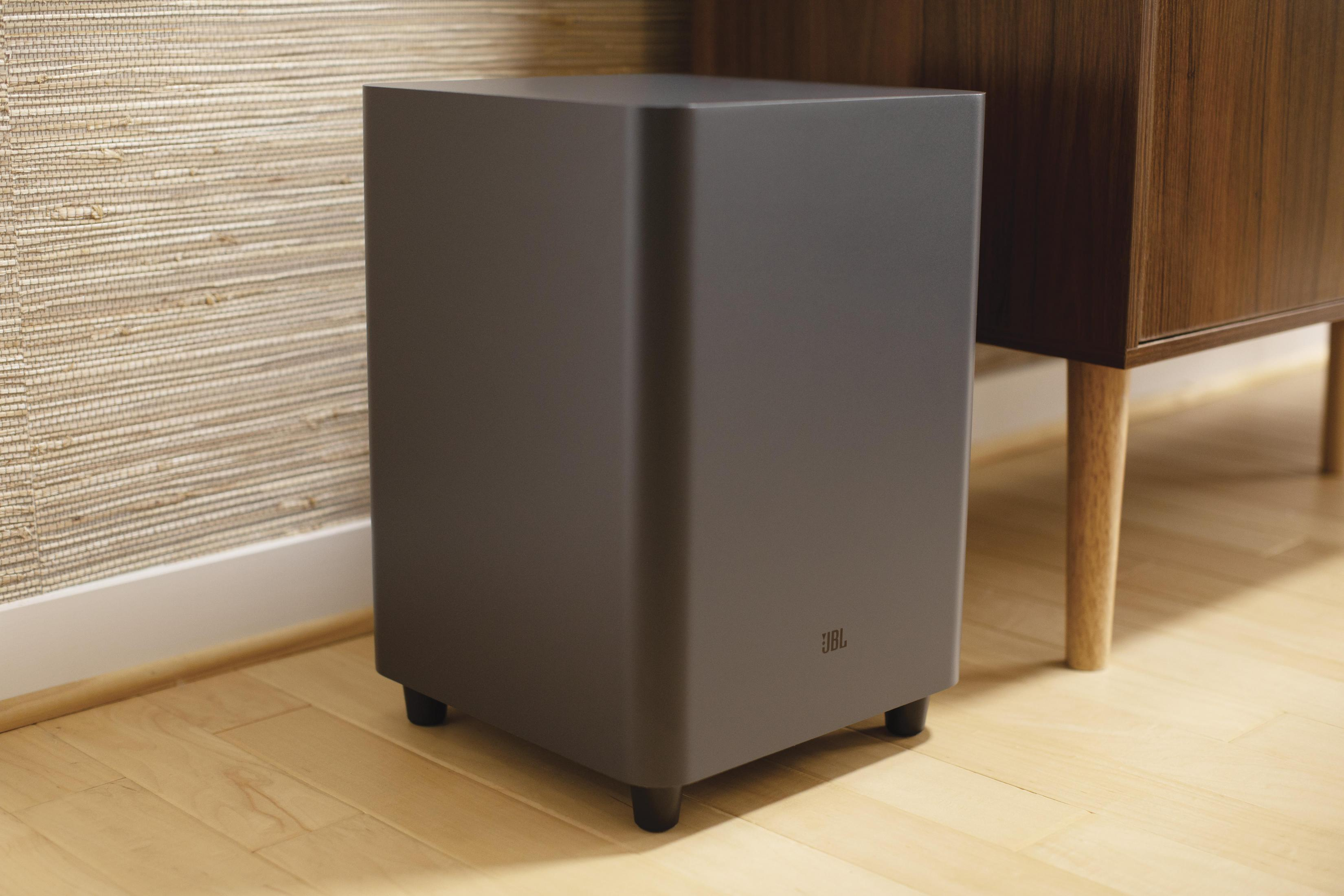 Ahşap zeminde, mobilyaların yanında siyah JBL subwoofer.