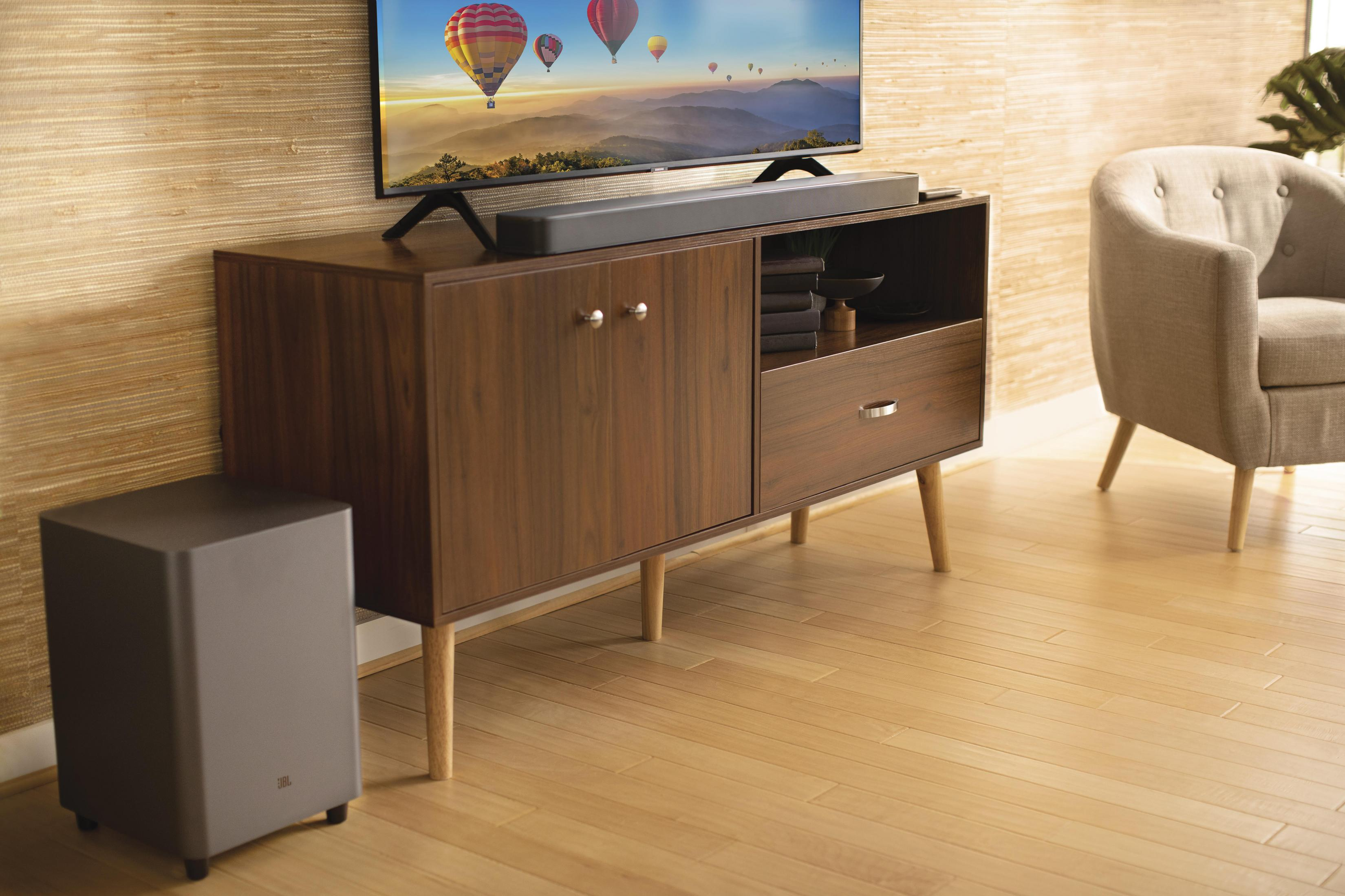 Ahşap bir dolap üzerinde TV ve soundbar ile subwoofer.