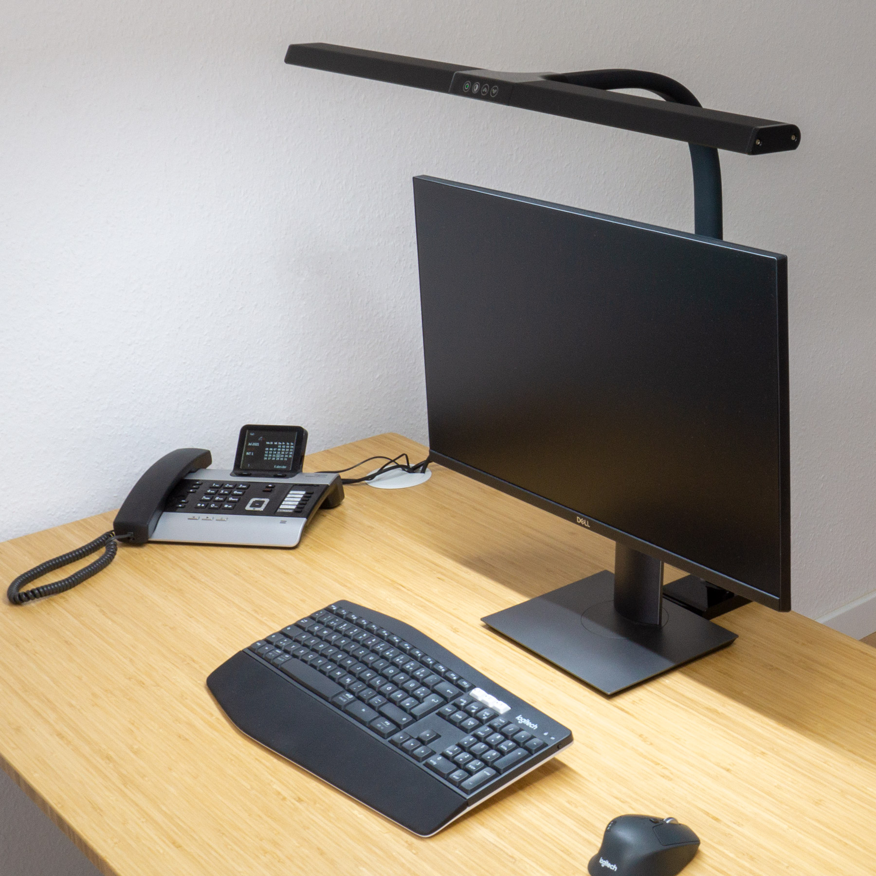 Ein Schreibtisch mit Monitor, Lampe, Tastatur, Telefon und Maus.