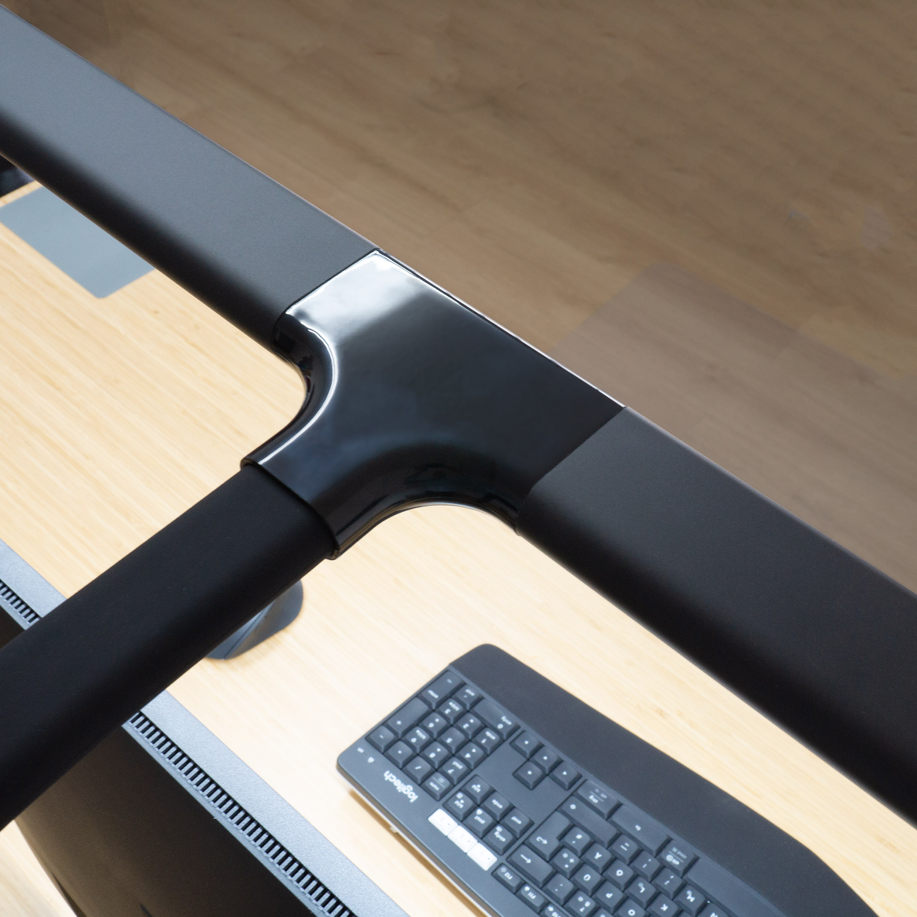 Schwarzer Monitorhalter mit Tastatur auf einem Holztisch.