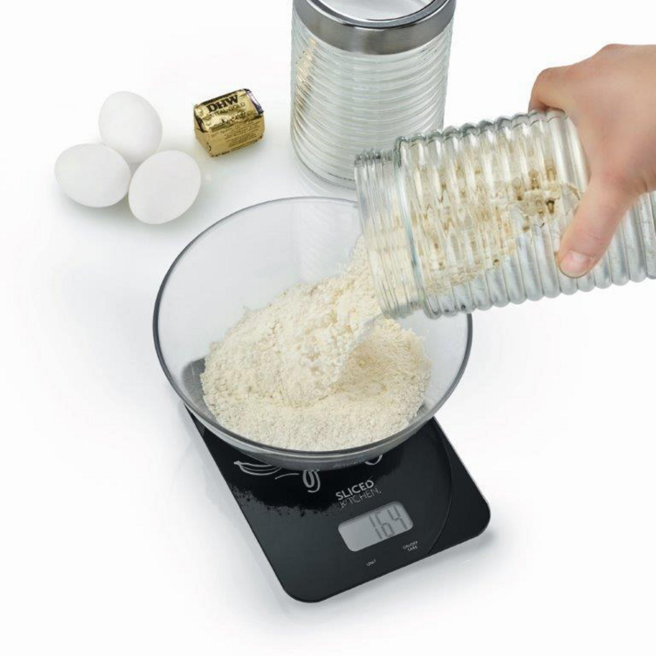 Osoba wsypuje mąkę do miski na wadze, obok jajka i masło.