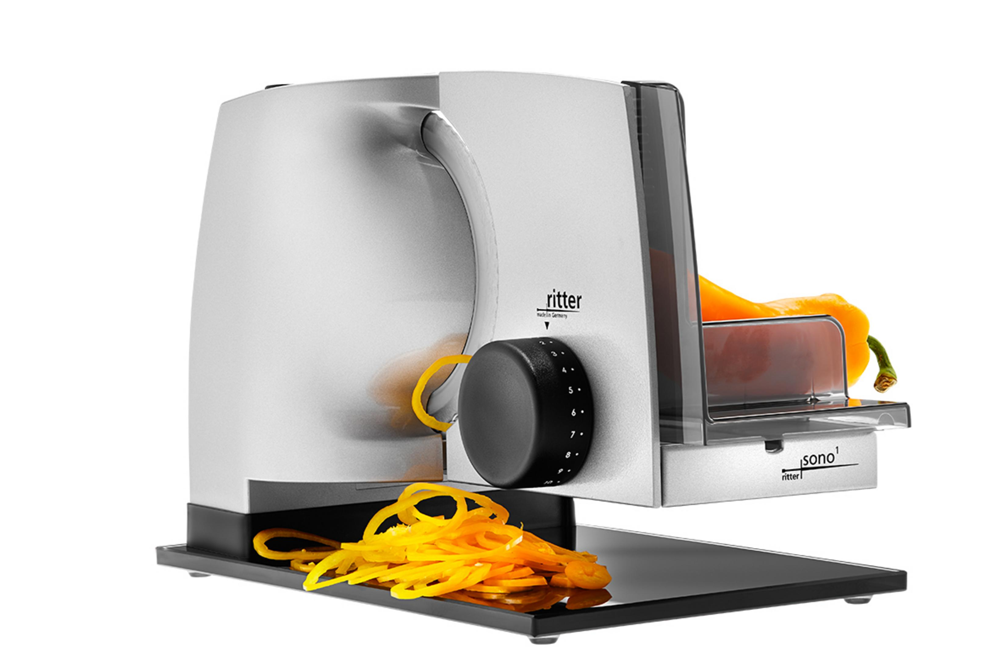 Srebrno-czarna krajalnica do żywności, z żółtą żywnością i czarną podstawą na białym tle.