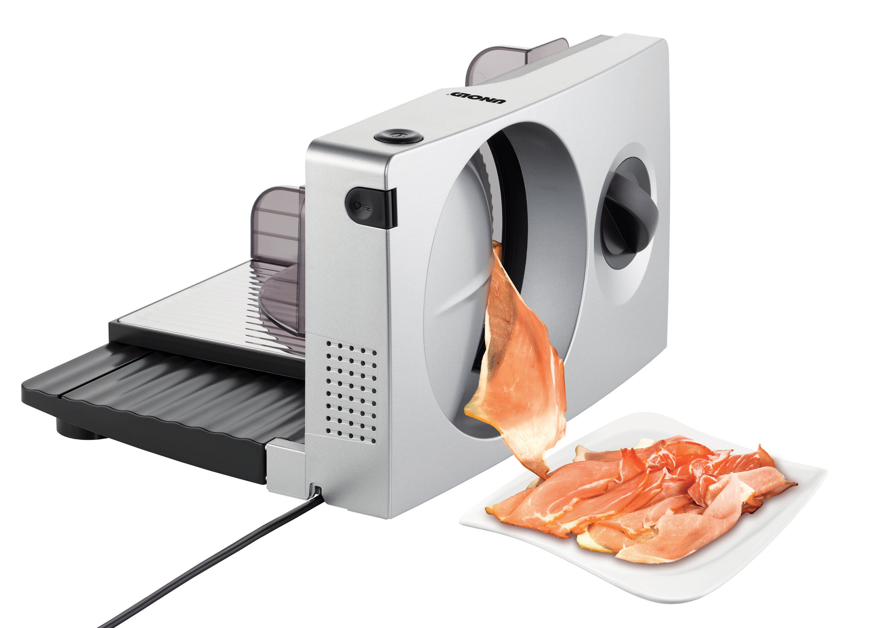 Krajarka do żywności z plasterkiem szynki. Biała maszyna, czarna podstawa, talerz z szynką.