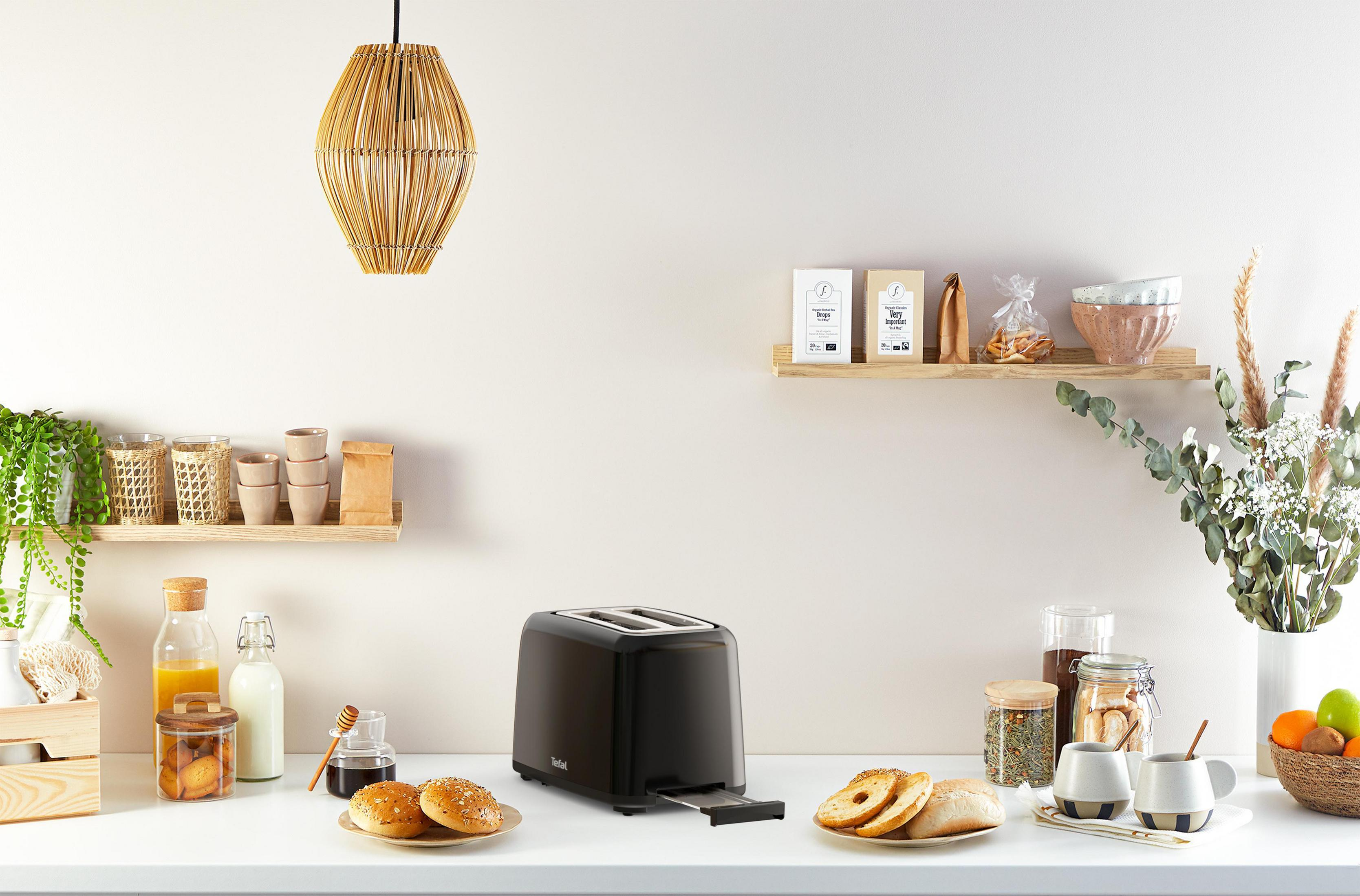 Küchenszene mit einem schwarzen Toaster, Lebensmitteln und Dekorationen auf weißer Oberfläche.