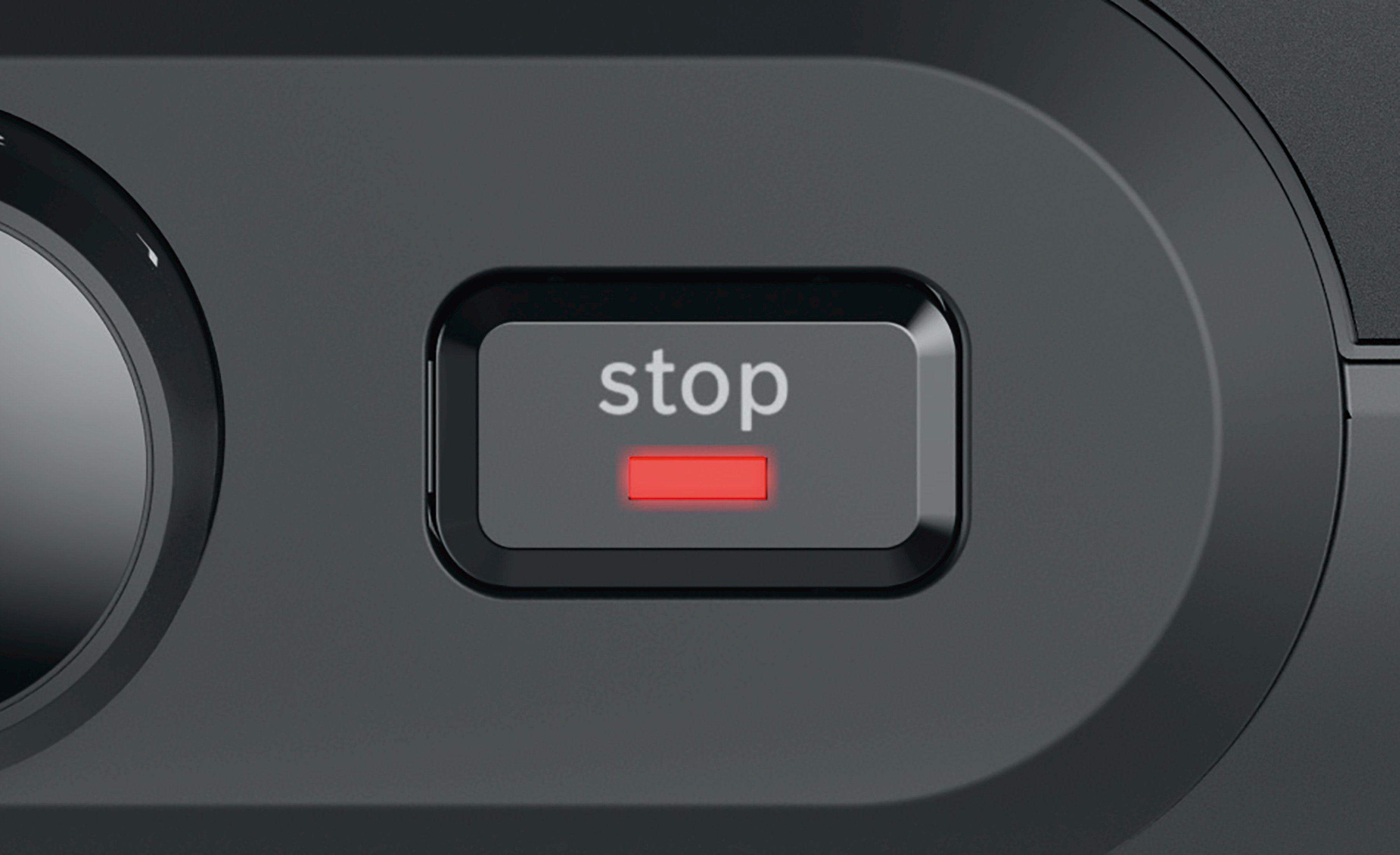 Zbliżenie czarnego przycisku z napisem „stop” w kolorze białym i czerwoną lampką kontrolną.