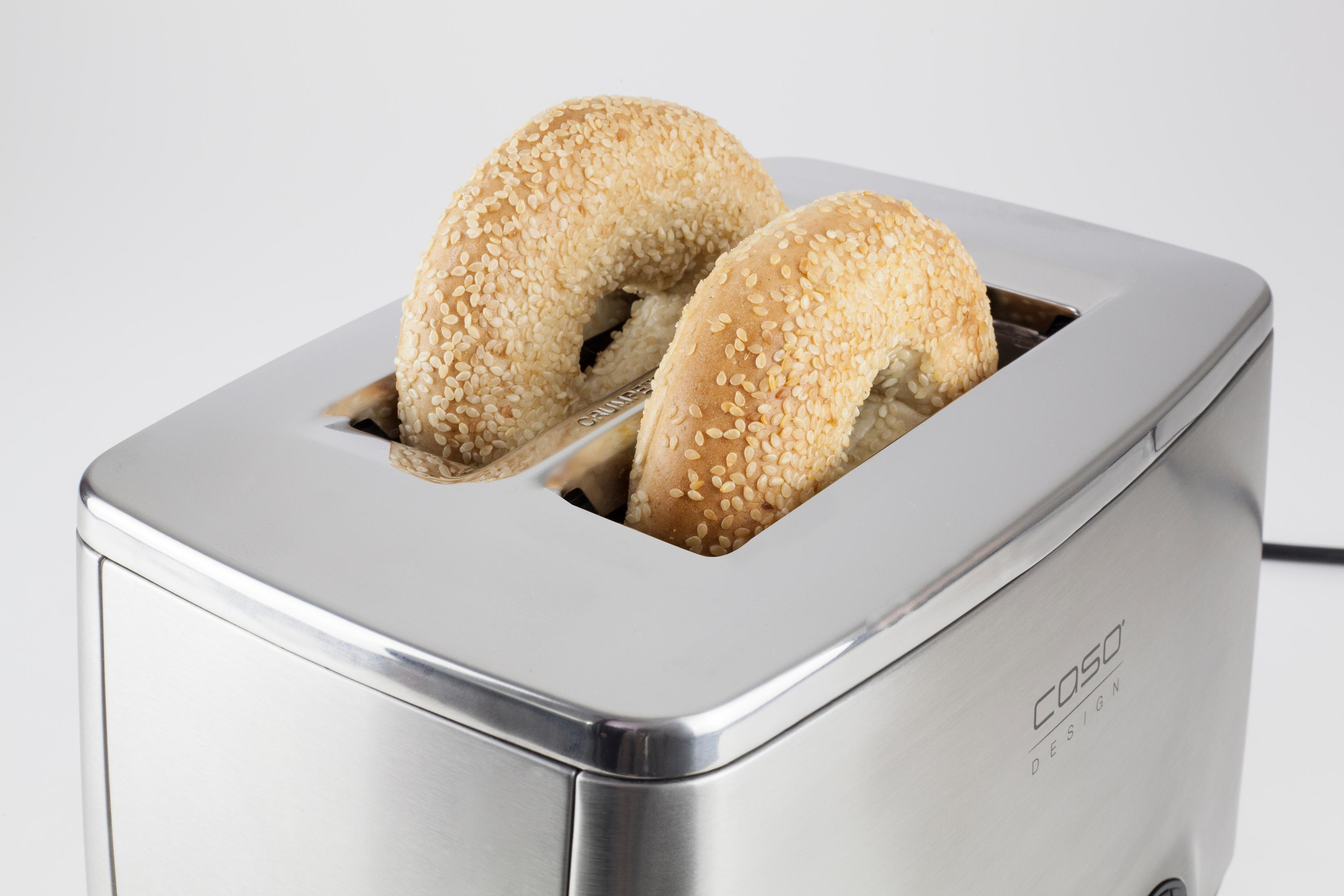 Una tostadora de acero inoxidable con dos bagels de sésamo dentro, sobre un fondo blanco.