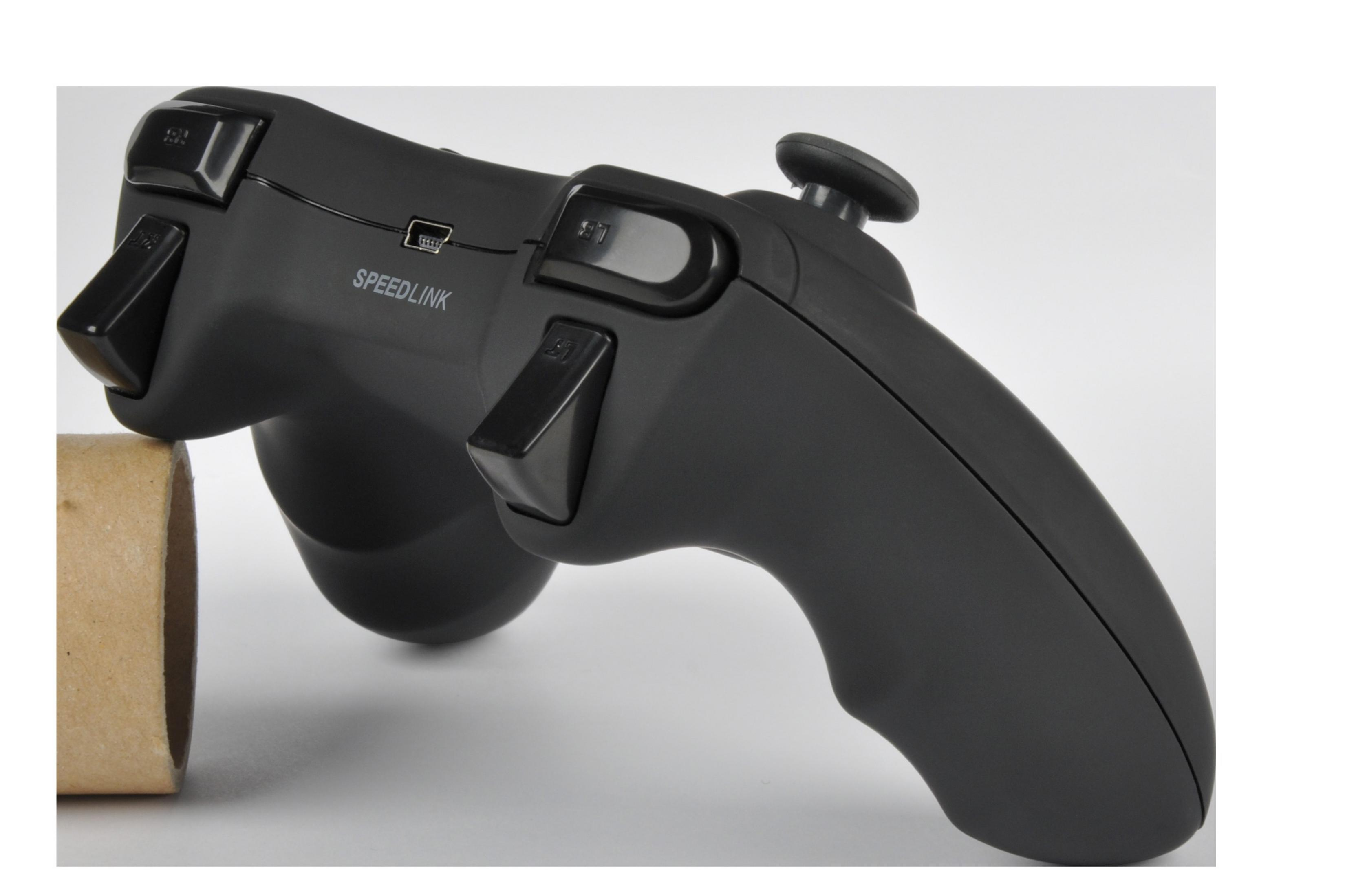 Czarny gamepad Speedlink. Posiada przyciski, joystick i port USB. Leży na białej powierzchni.