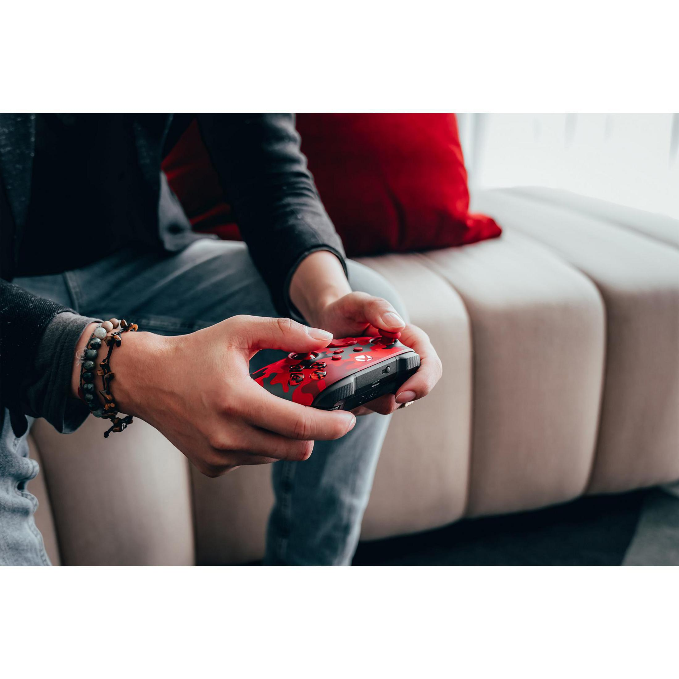 Eine Person hält einen rot-schwarzen Controller und sitzt auf einer beigen Couch.