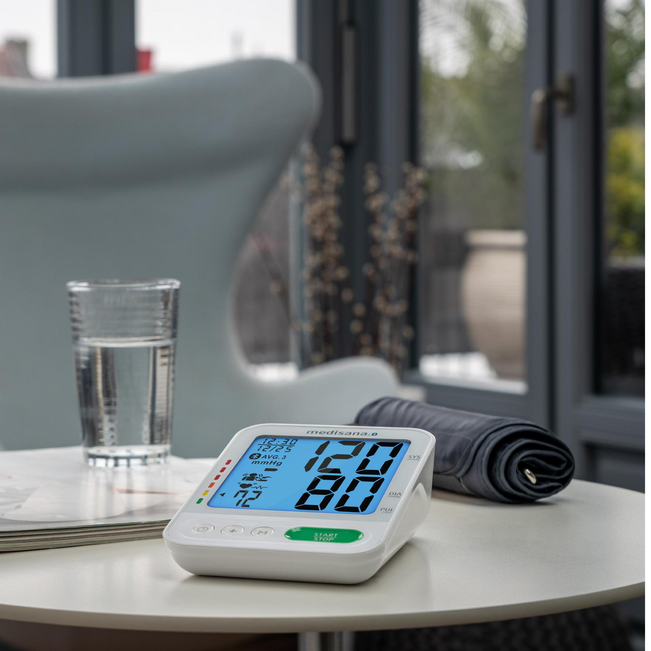 Ciśnieniomierz na białym stole. Szklanka wody i zwinięty mankiet są w pobliżu.