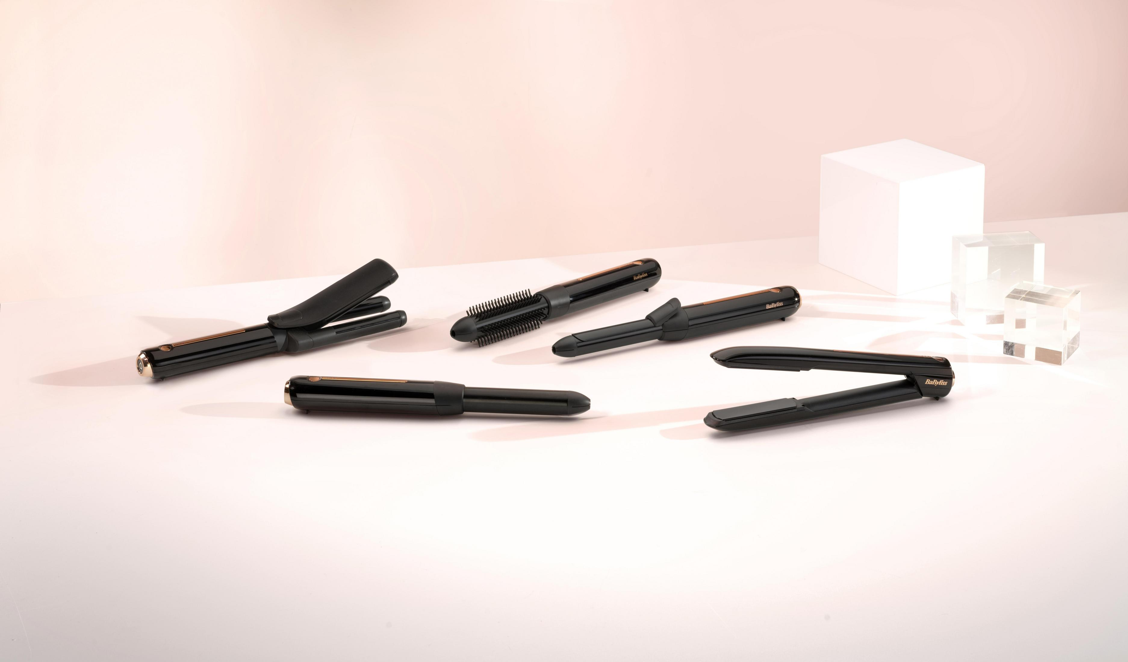Haarstyling-Tools auf hellrosa Oberfläche. Mehrere Lockenstäbe.