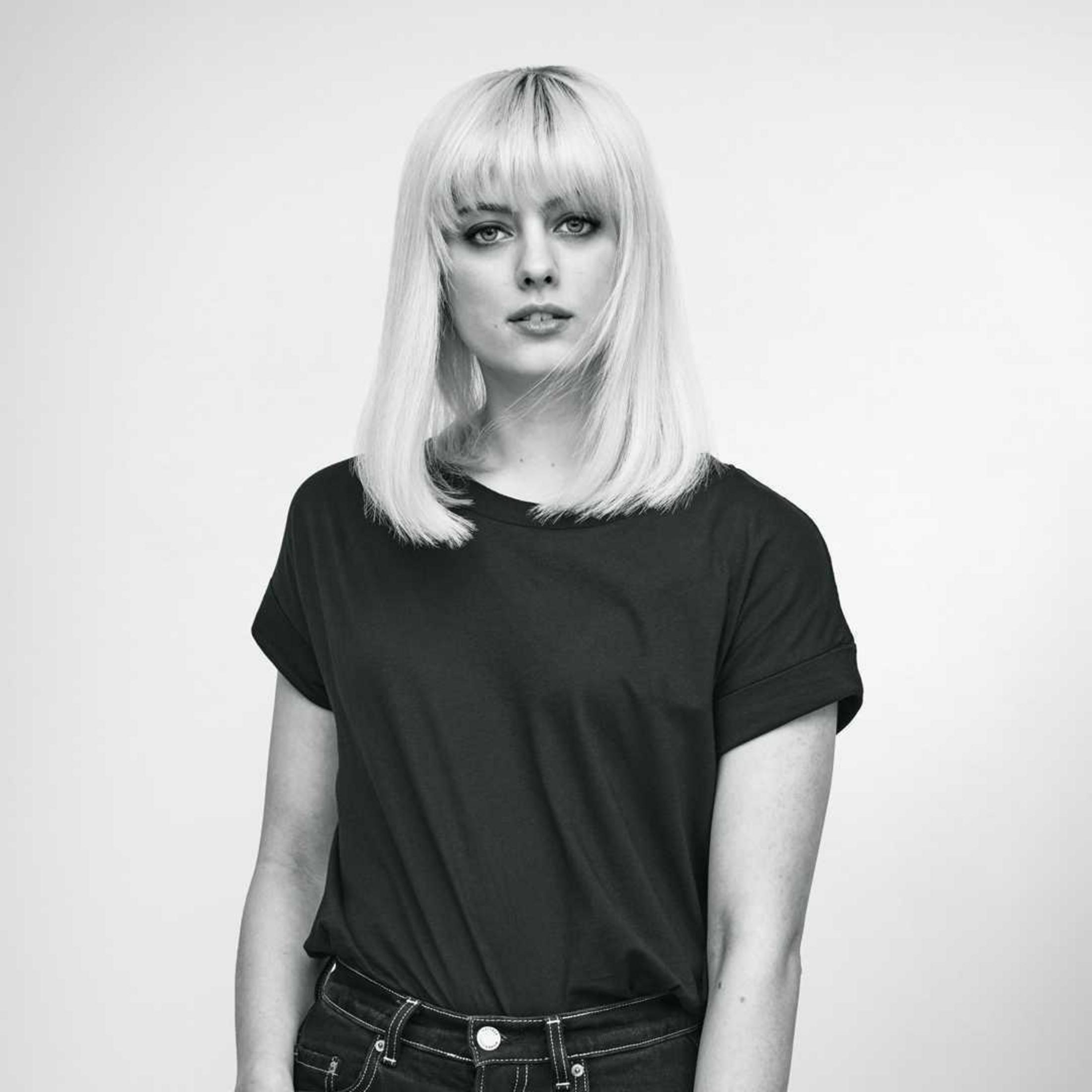 Kobieta z blond włosami, w czarnym t-shircie, w skali szarości.