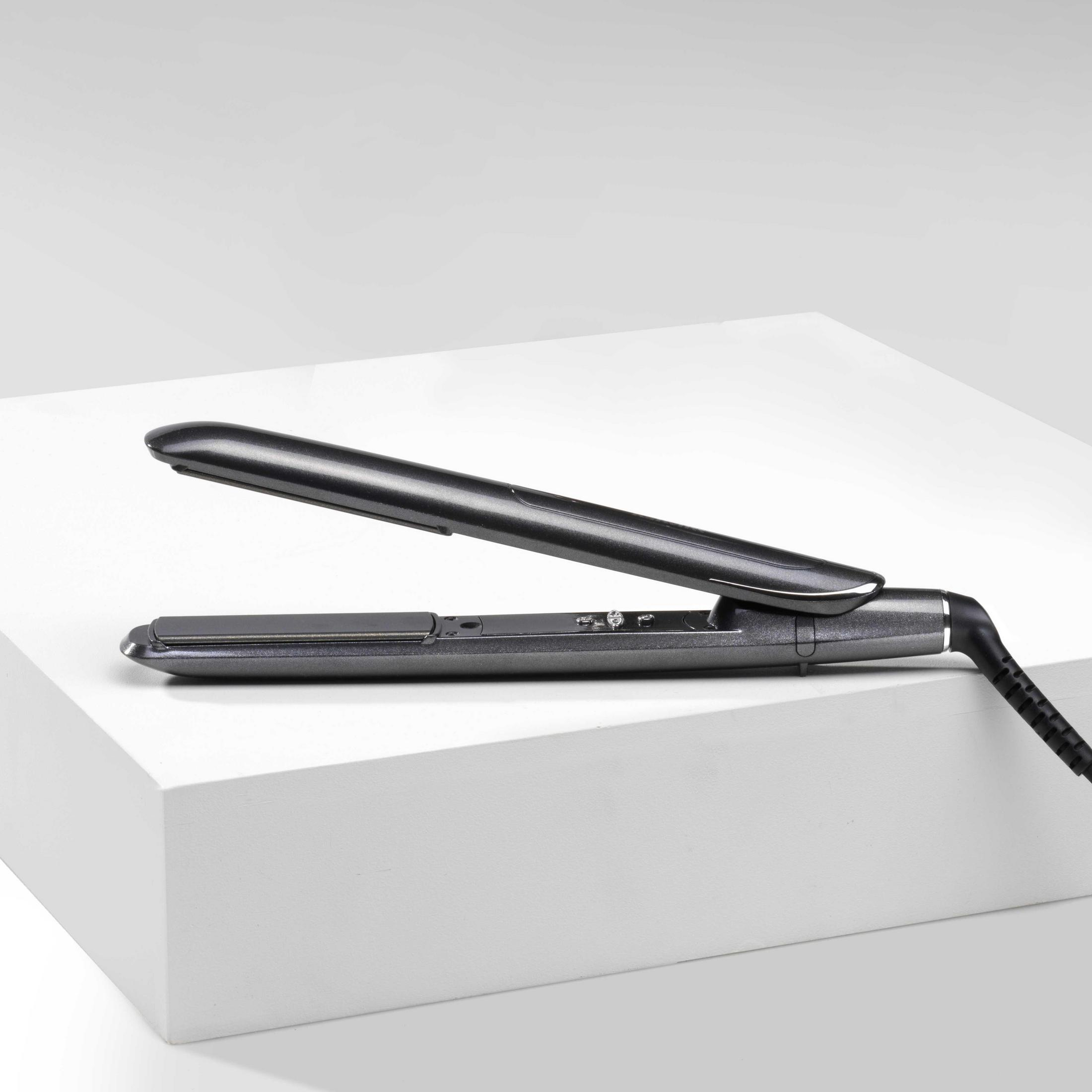 Ciemnoszara prostownica, otwarta, na białej platformie.