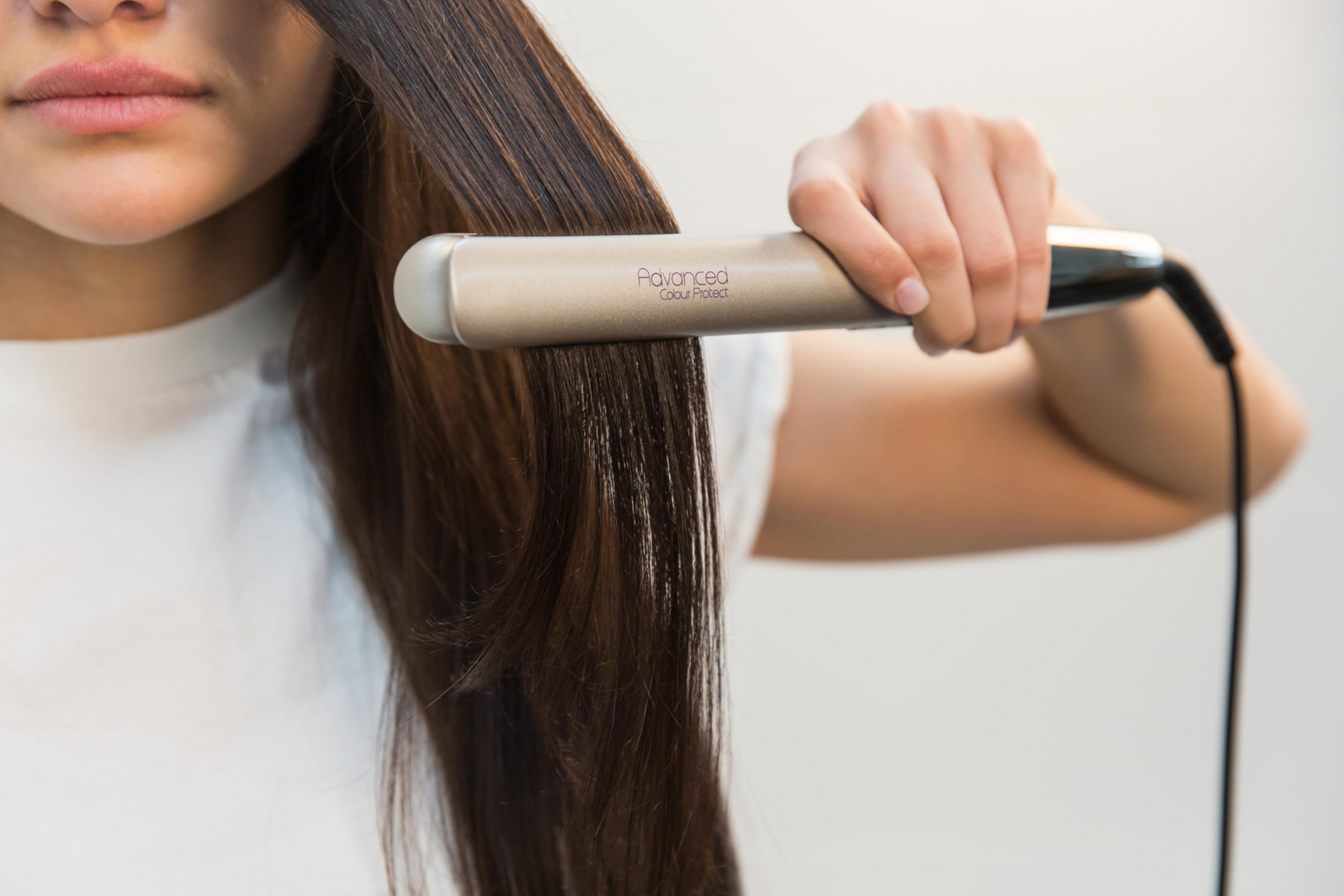Kobieta prostuje włosy beżową prostownicą na białym tle.