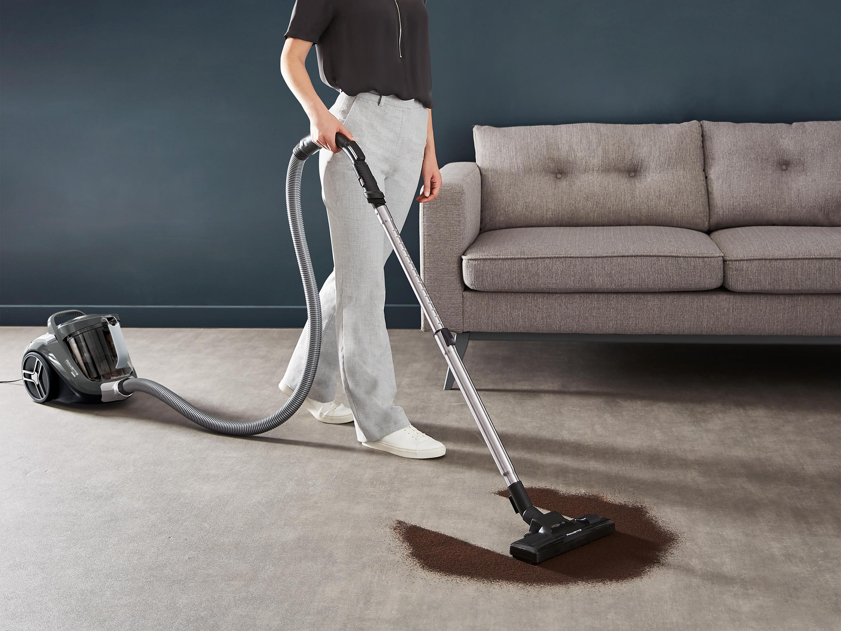 Eine Person, die einen dunklen Fleck auf einem Teppich in einem Wohnzimmer mit Sofa saugt.