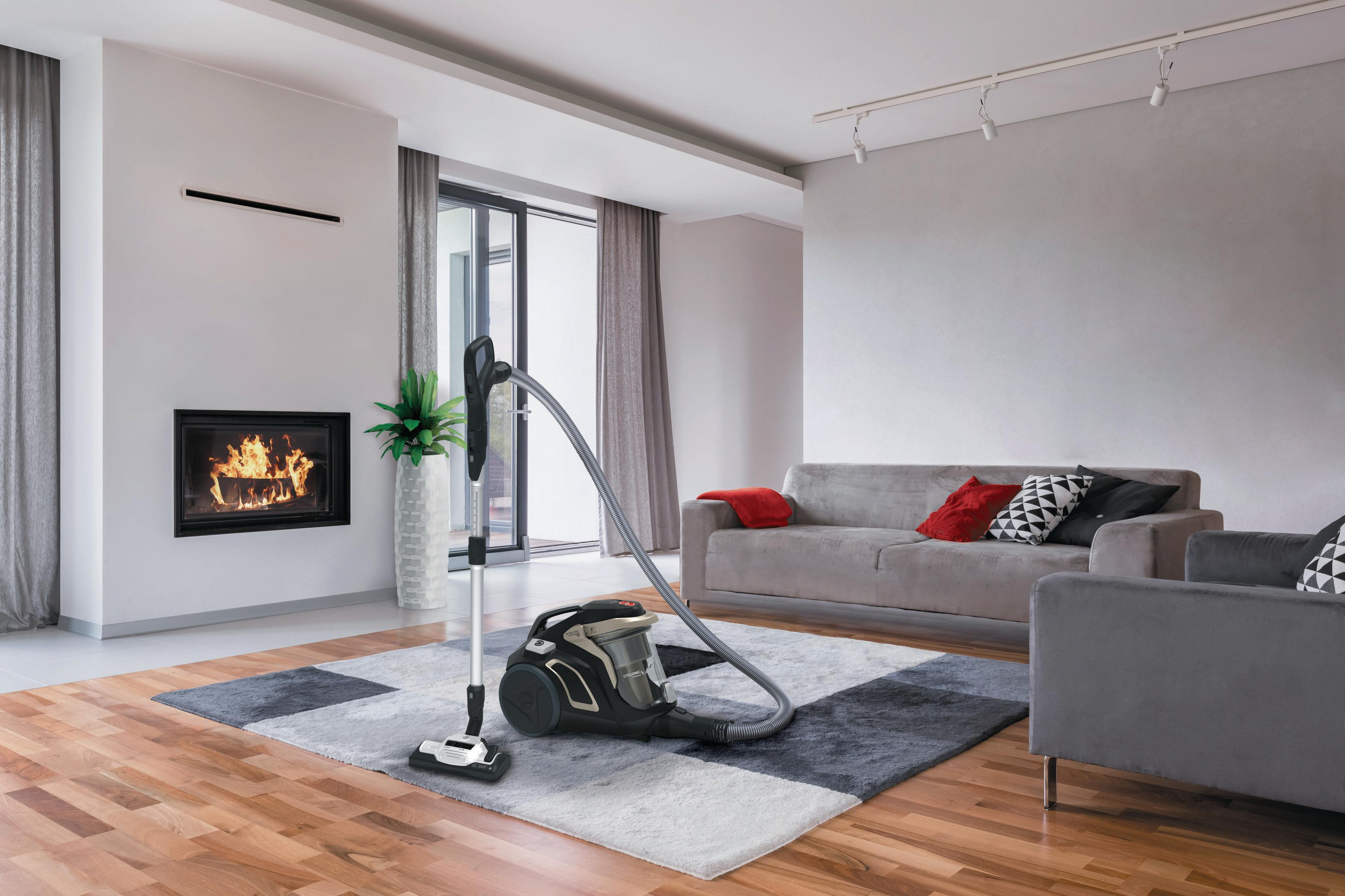 Salon z odkurzaczem, sofą, kominkiem i dywanem. Nowoczesny wystrój wnętrz z drewnianą podłogą.