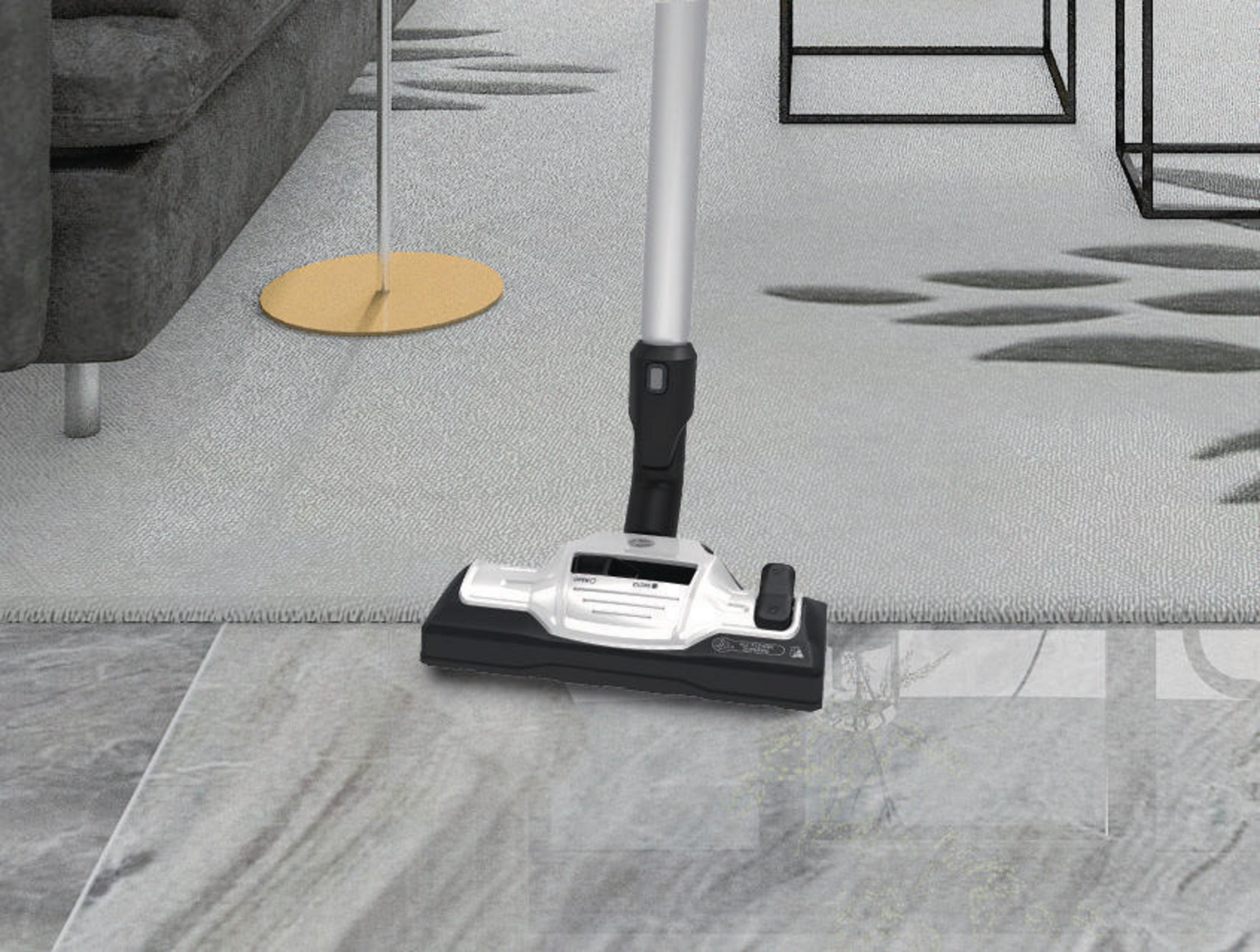 Głowica odkurzacza na jasnej podłodze, z sofą i zasłoną w tle.