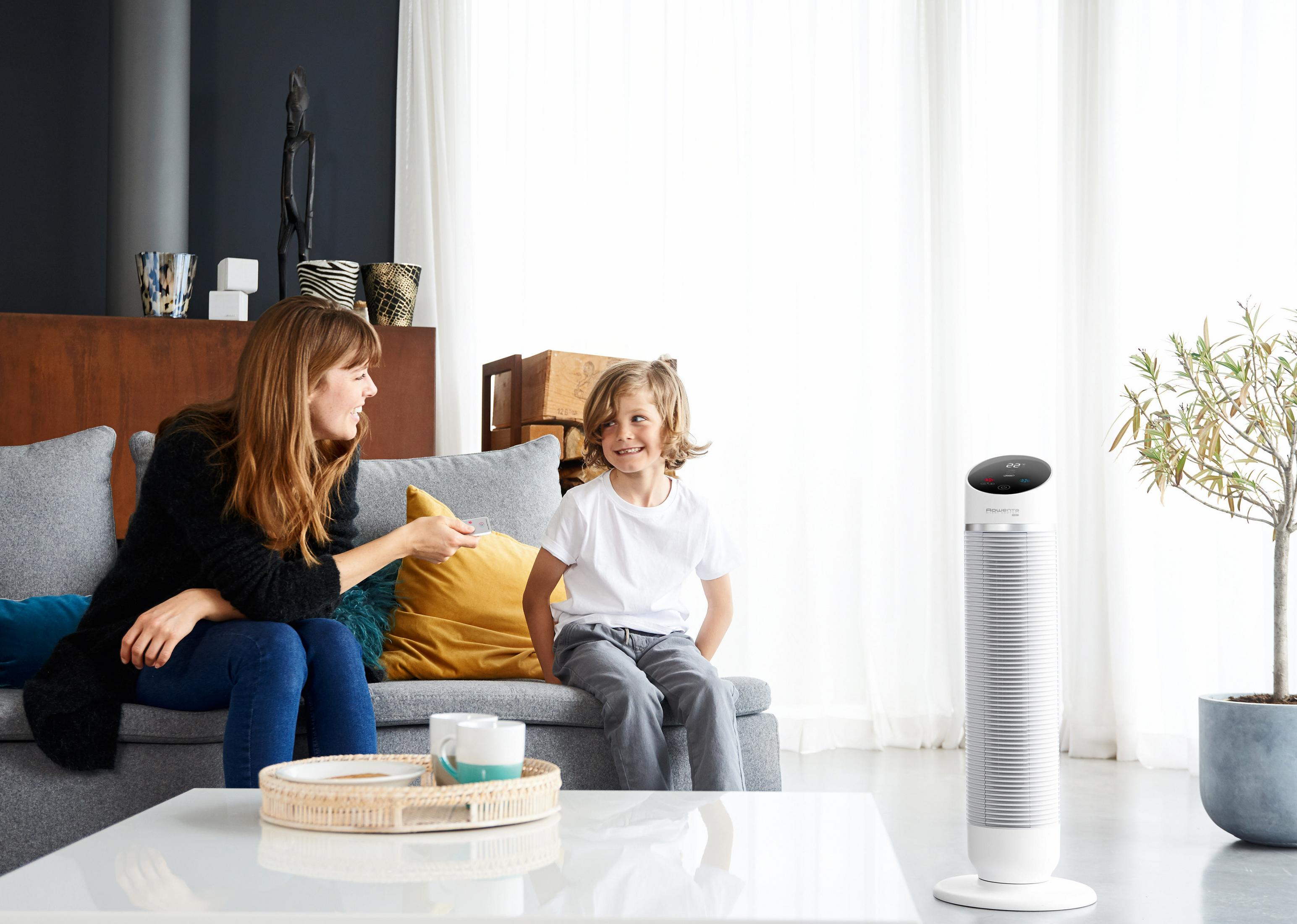 Kobieta i dziecko siedzą w pobliżu białego wentylatora i stolika kawowego.