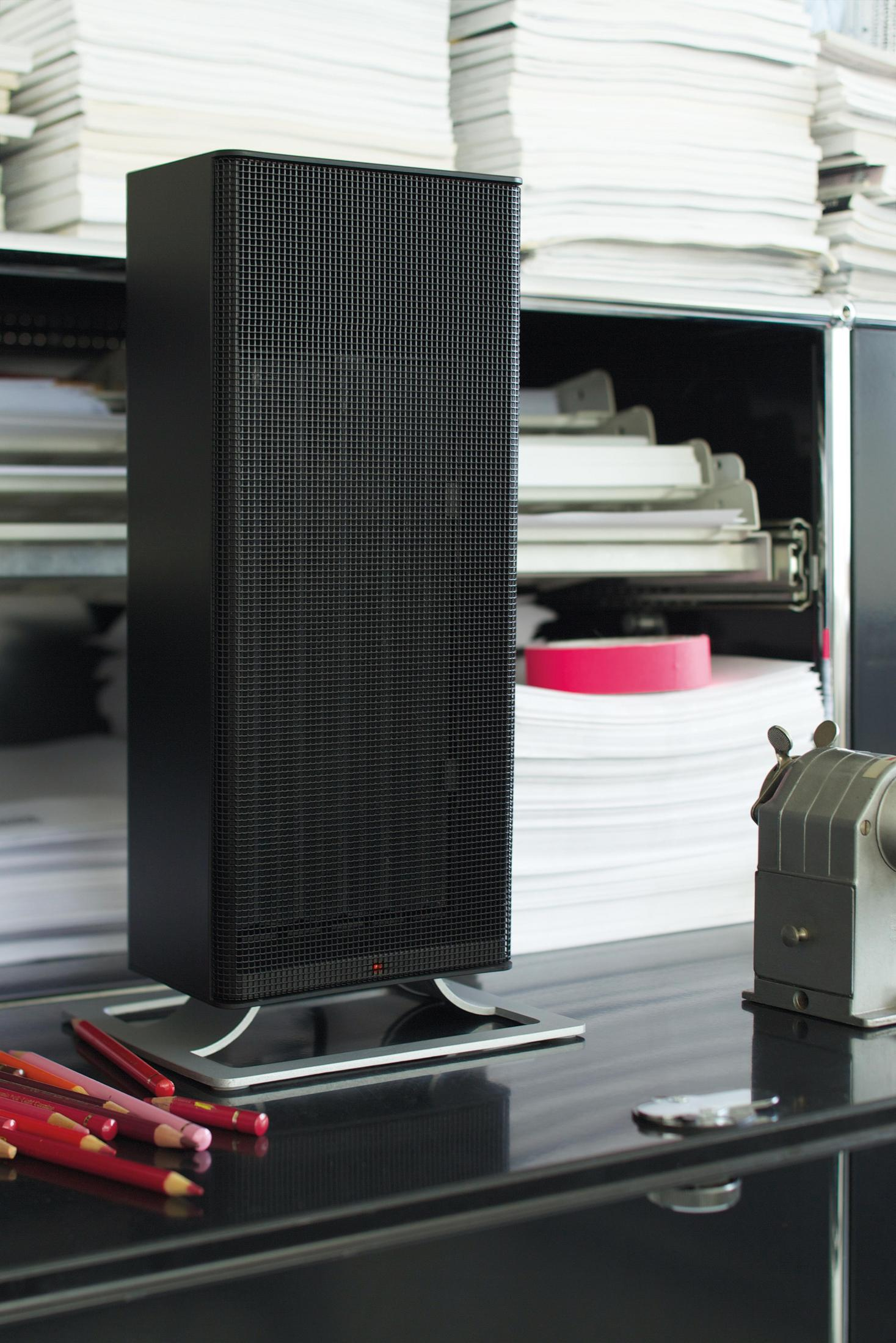Haut-parleur noir sur un bureau. Des crayons rouges et un taille-crayon sont visibles. Documents en arrière-plan.