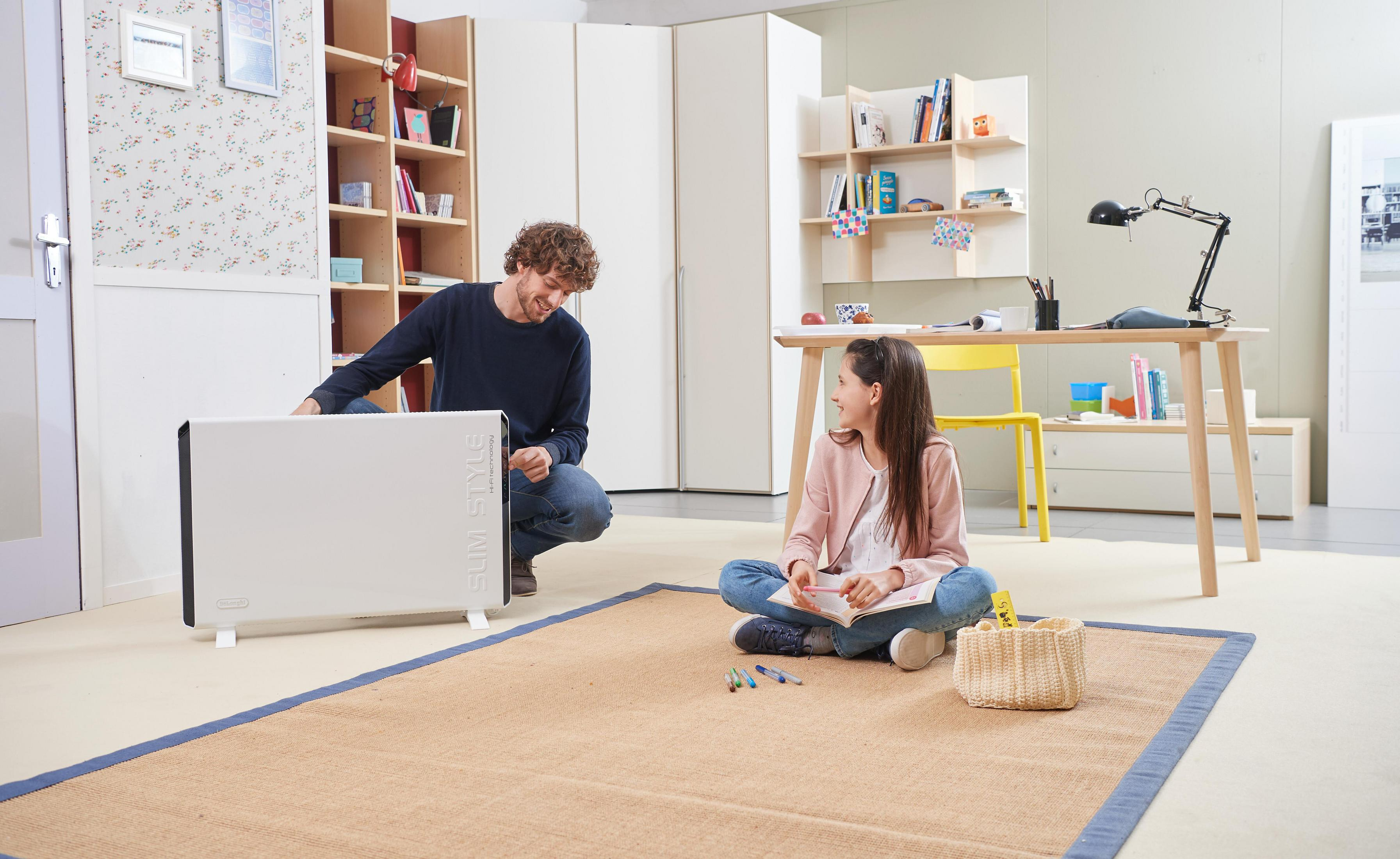 Ojciec i córka w pobliżu białego grzejnika na dywanie. Są w pokoju z regałem na książki.