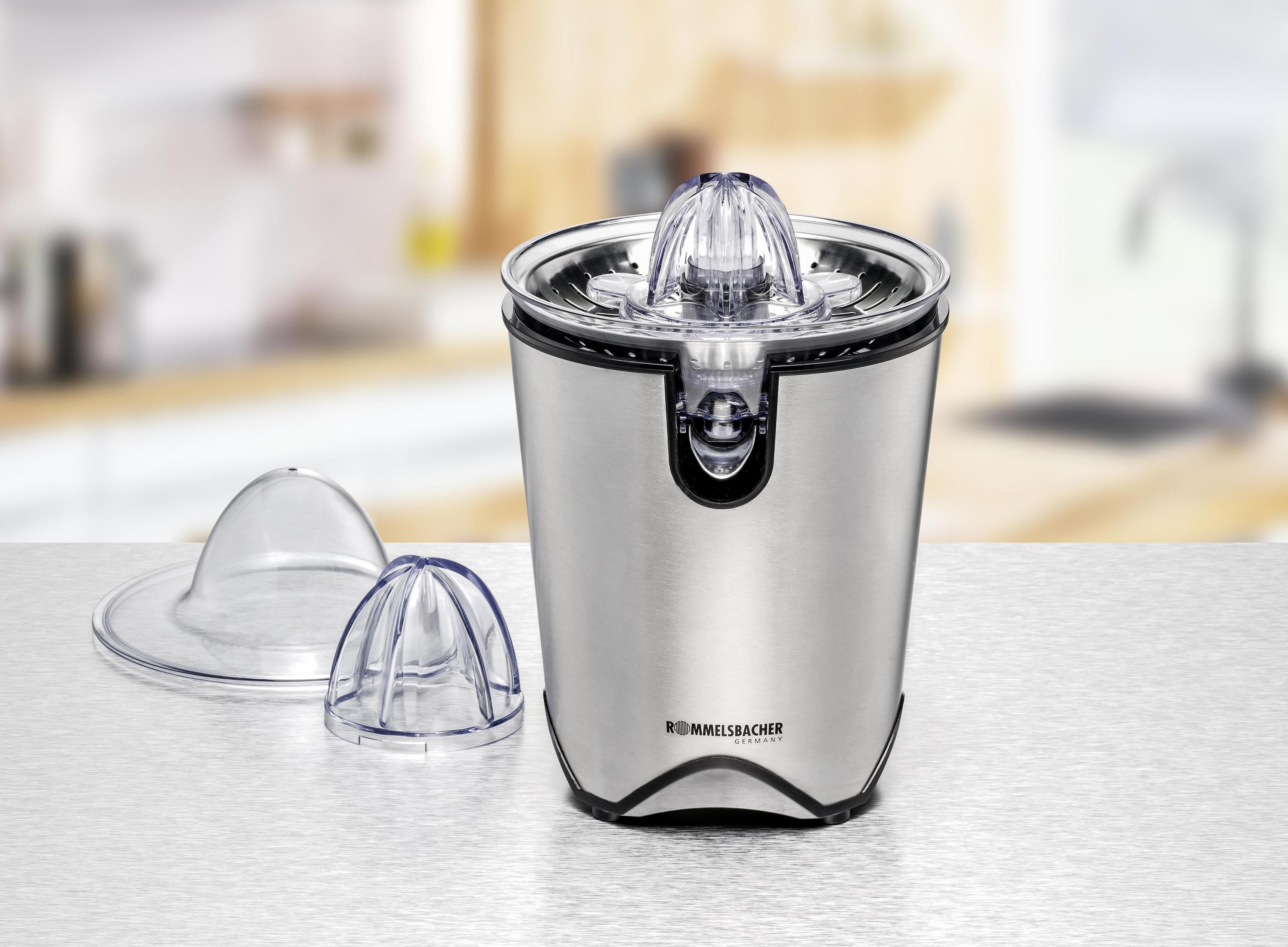 A stainless steel juicer with parts on a white surface. The background is blurry.