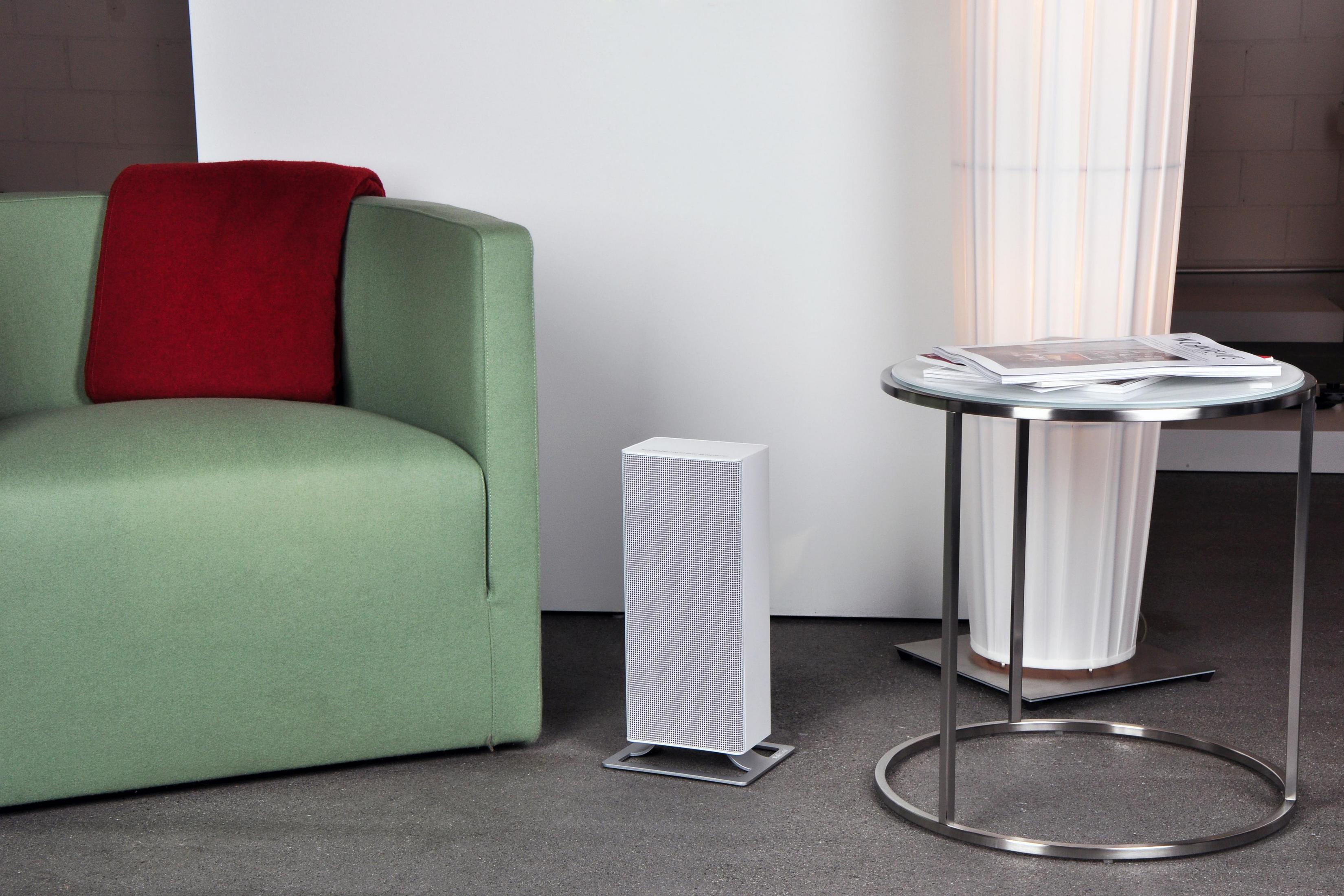 Scena w salonie z zieloną sofą, białym głośnikiem i okrągłym stołem. Szara podłoga, biała ściana.