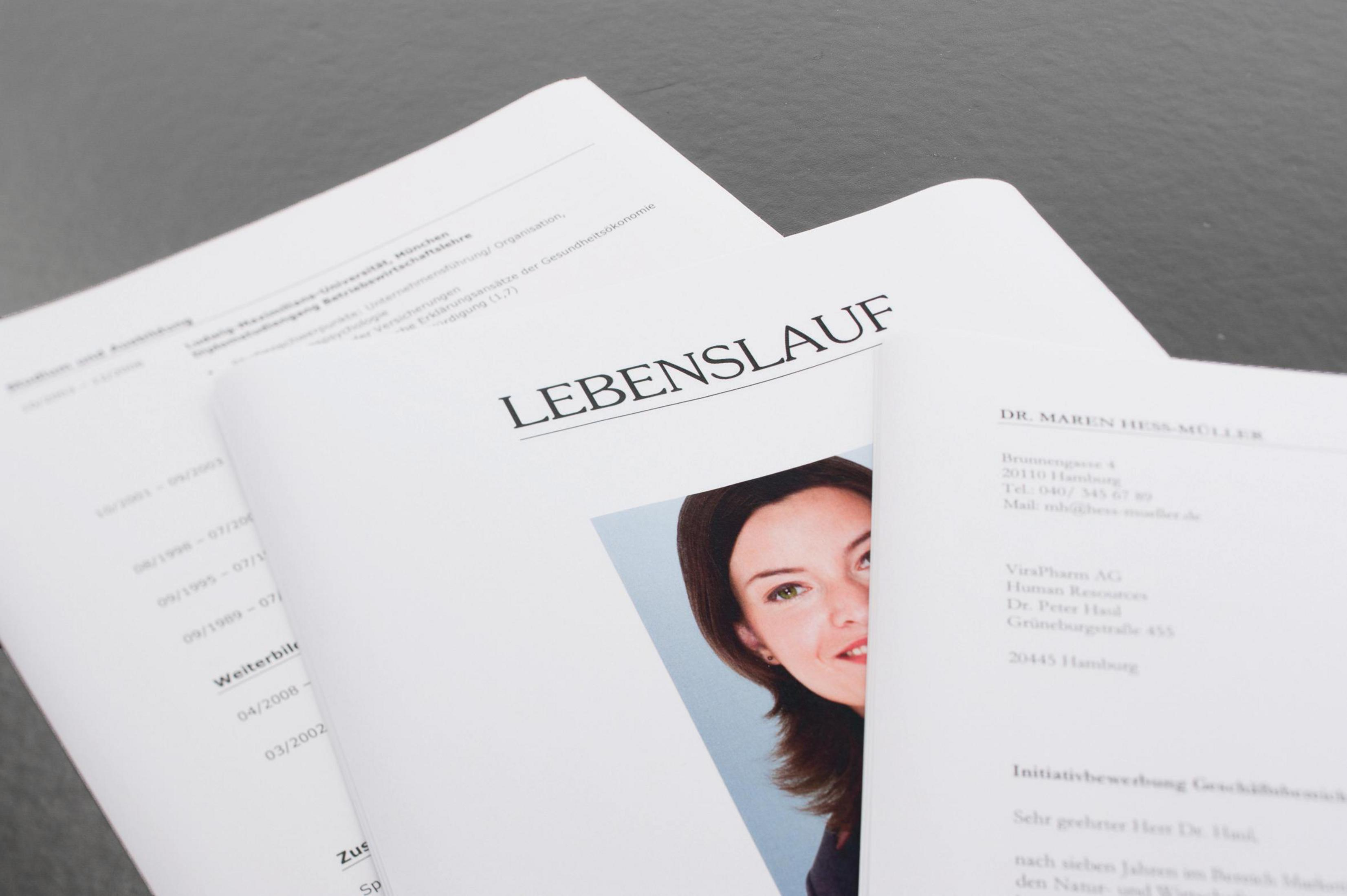 Papier mit Text und einem Frauengesicht. Das Wort 'Lebenslauf' ist sichtbar. Dokumente gestapelt.