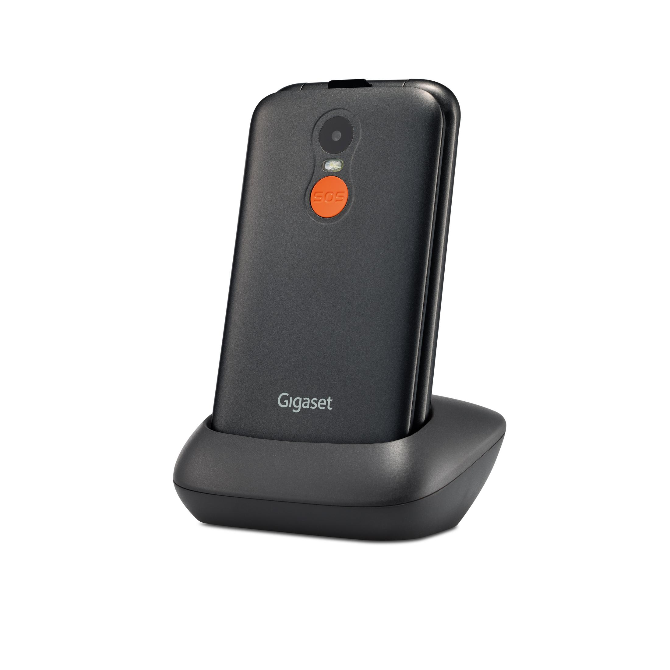 Un telefono a conchiglia Gigaset grigio si trova nella sua base di ricarica nera. Il retro del telefono ha una fotocamera e un pulsante SOS arancione.