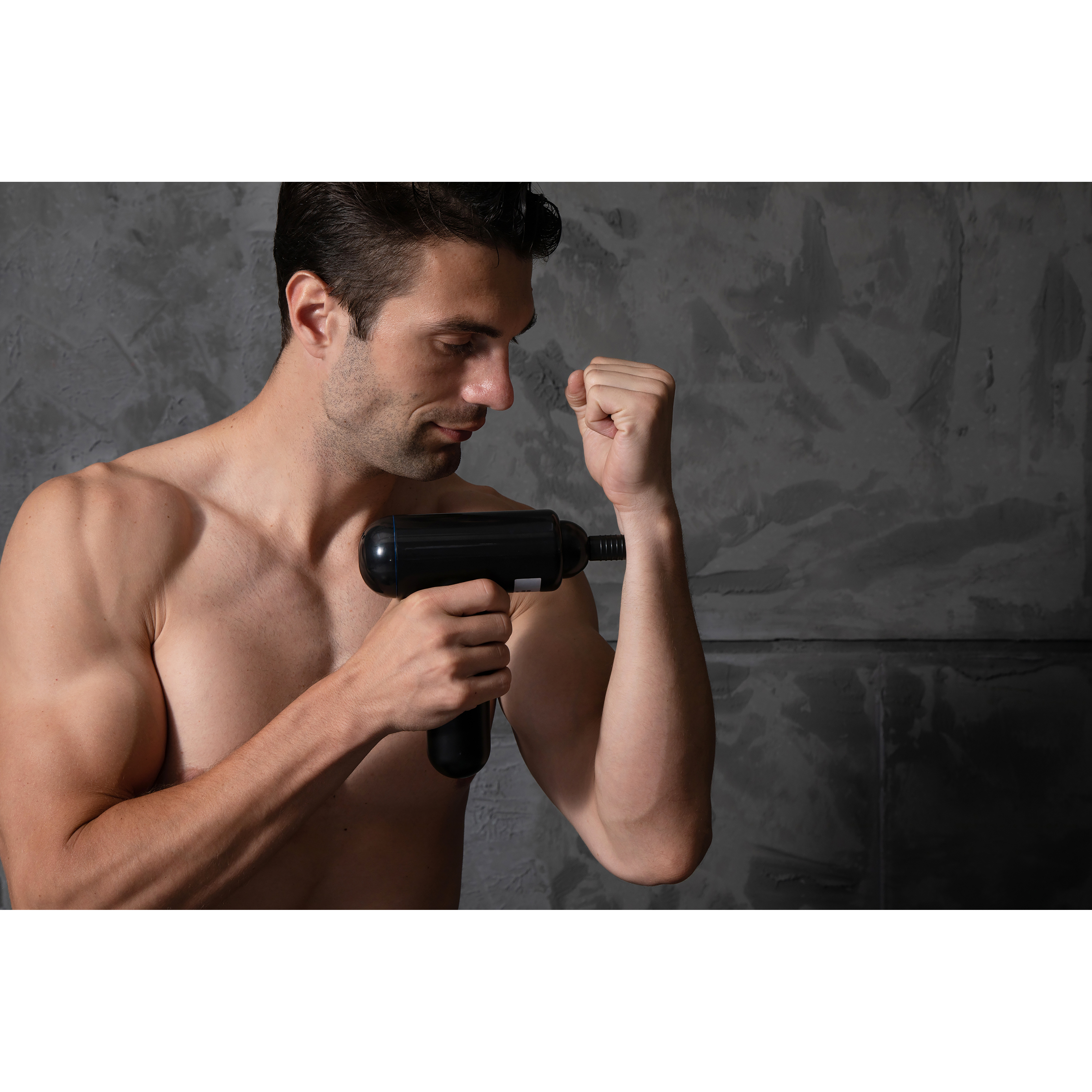 Mężczyzna używa pistoletu do masażu na ramieniu. Szara ściana w tle.