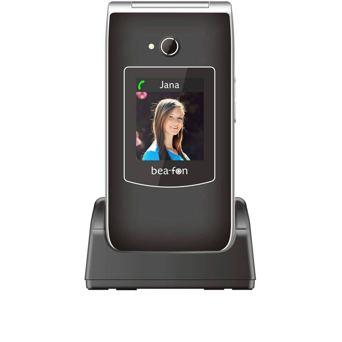 Un teléfono plegable negro en una base de carga. La pantalla muestra una foto y el nombre Jana. La marca es bea-fon.