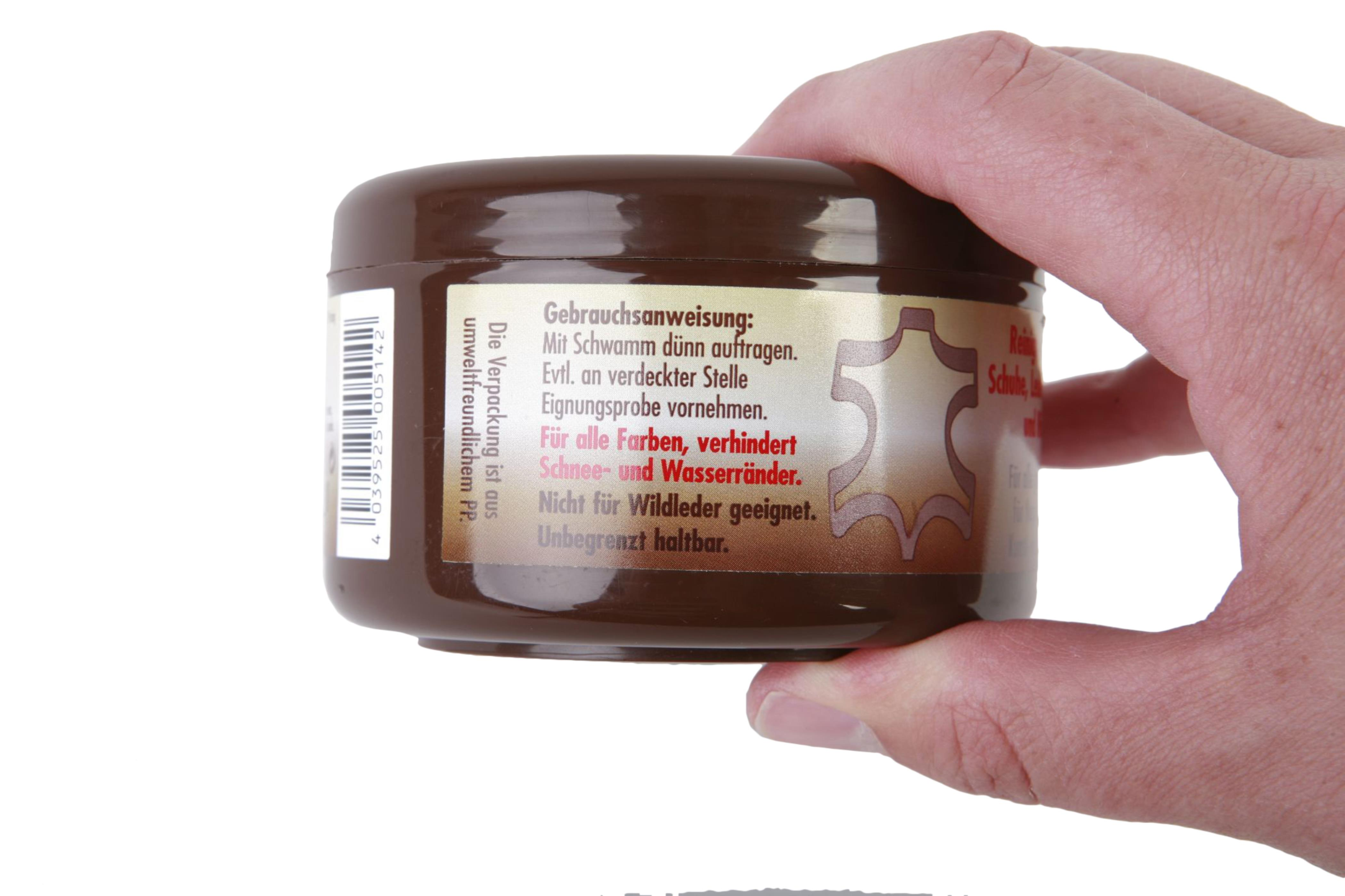 Ein Glas braune Schuhcreme. Es ist in einer Hand, mit Text in einer Fremdsprache darauf.