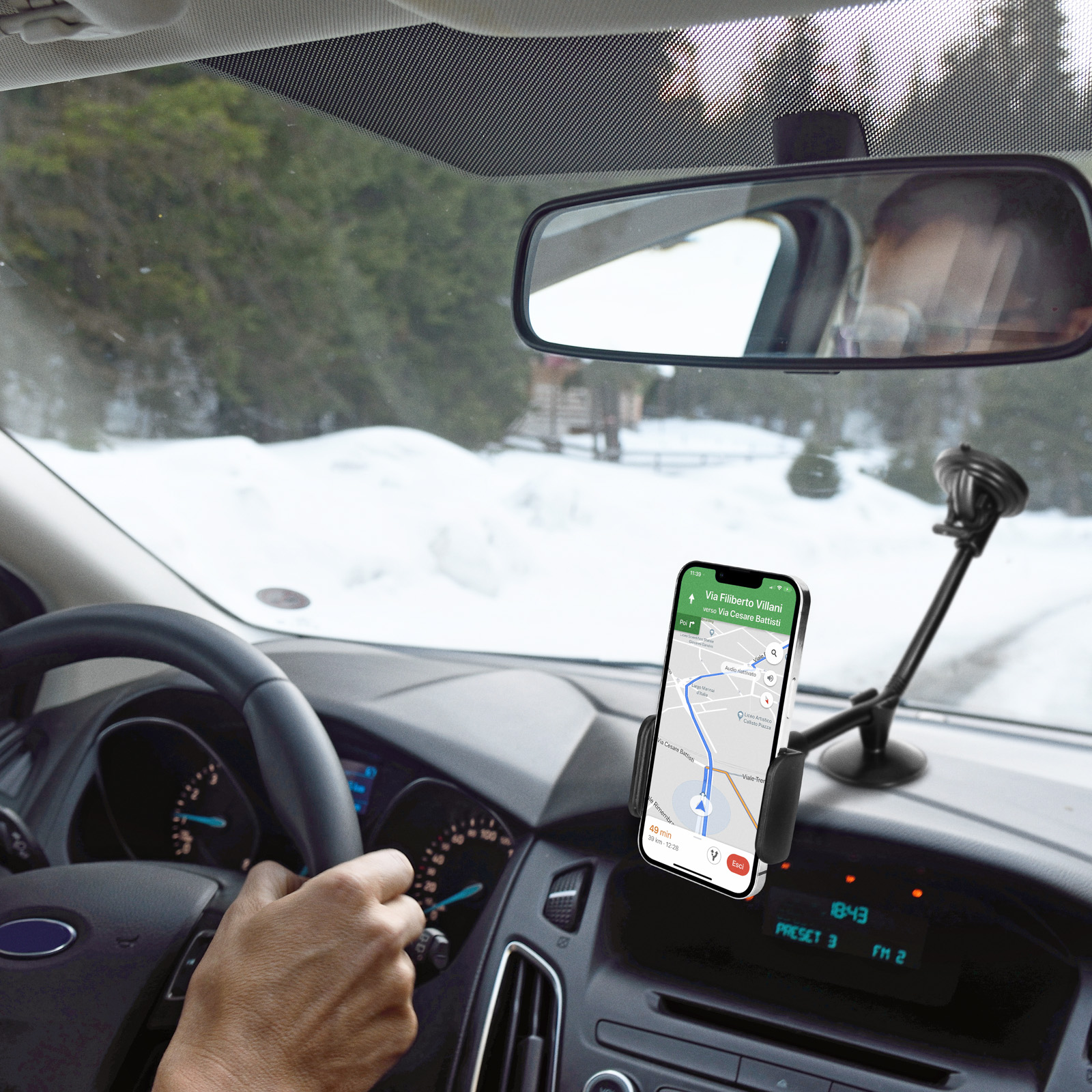 Auto-Innenraum. Telefon im Halter mit Karte. Lenkrad und Spiegel sichtbar. Schnee draußen.