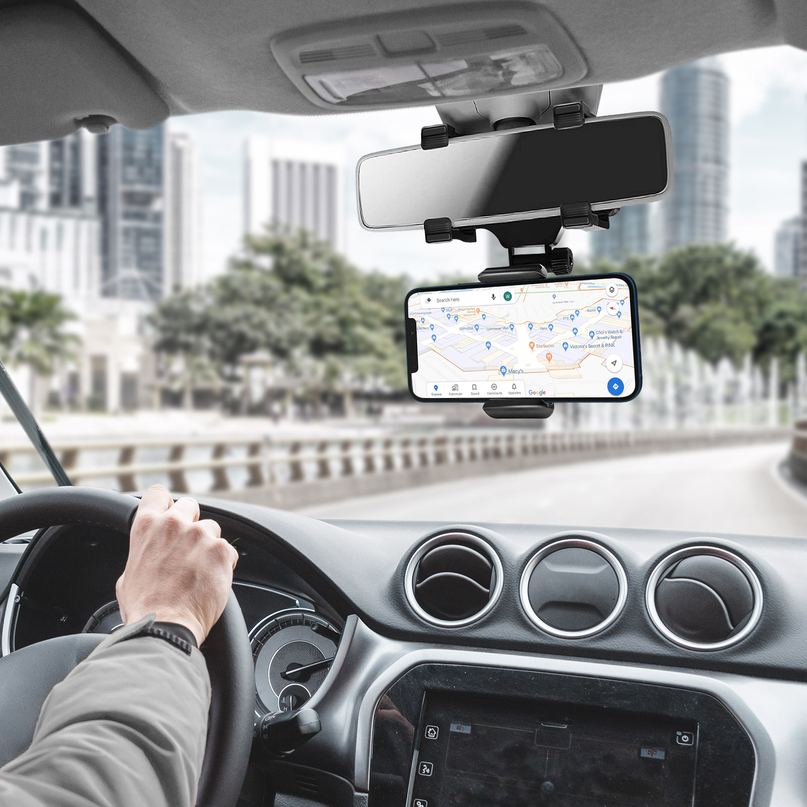 Mano sul volante, telefono con mappa montato, città sullo sfondo.