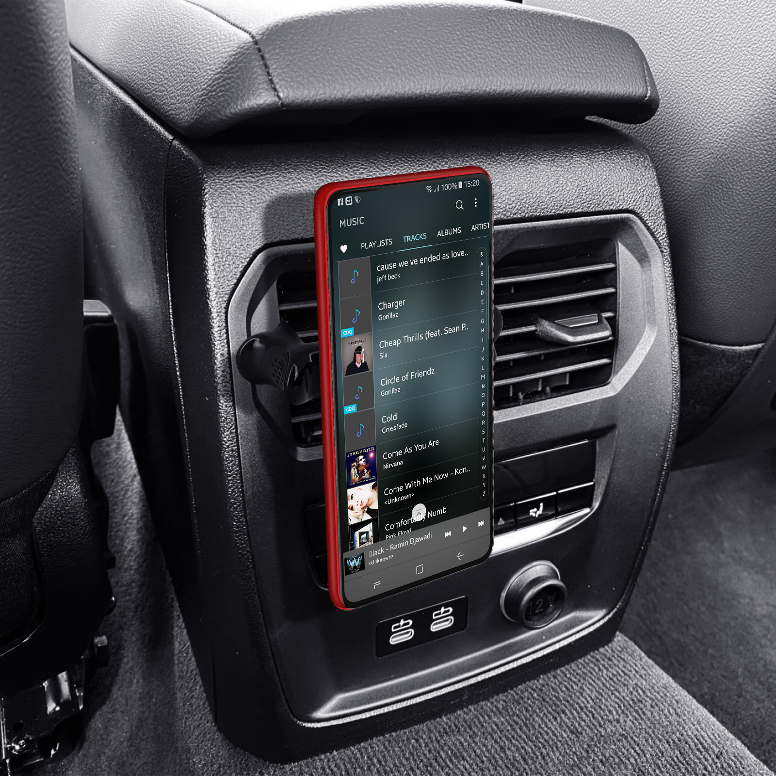 Telefon im Auto montiert, zeigt Musik-App und Ladeanschlüsse.