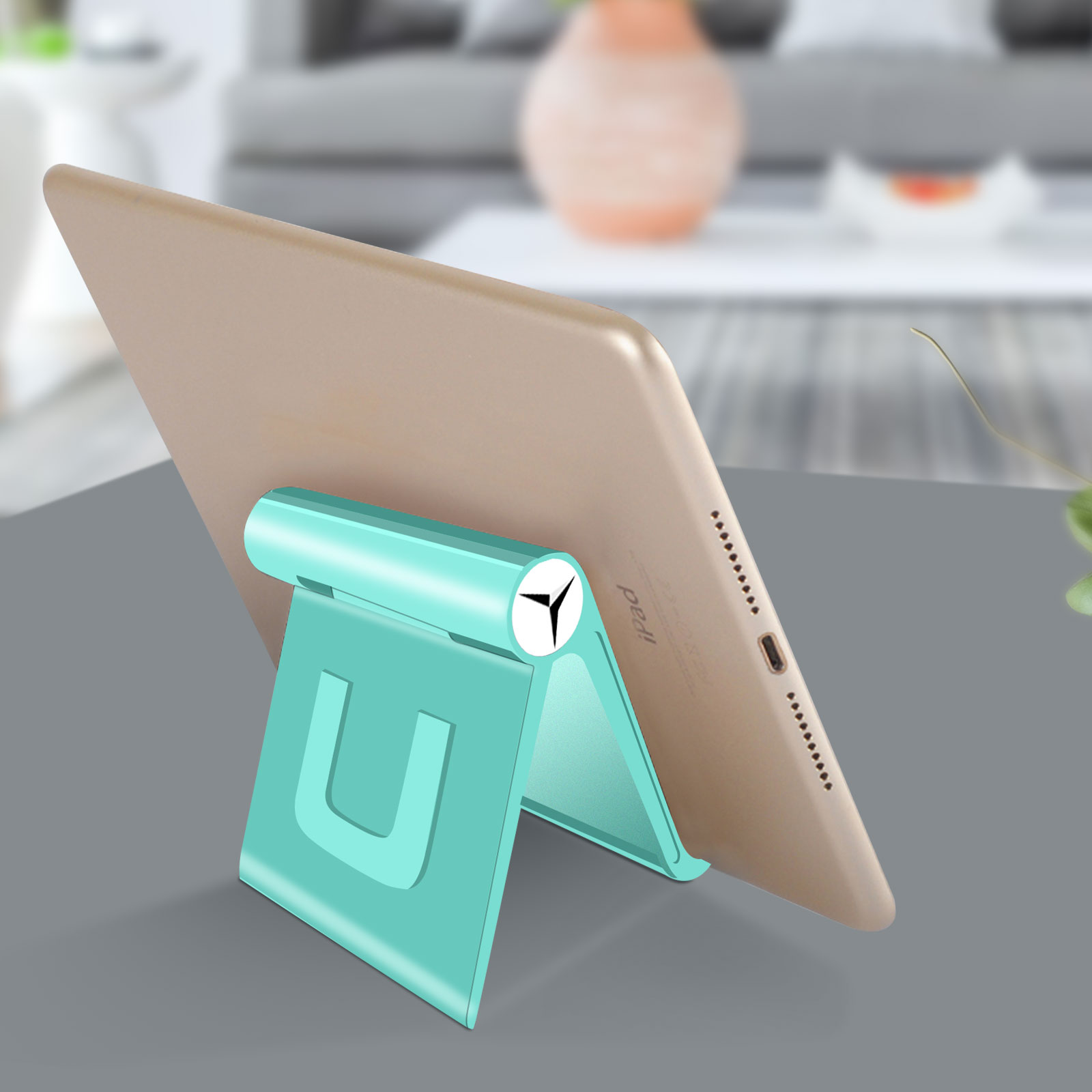Un supporto per tablet turchese che tiene un tablet dorato. Il supporto è su una superficie grigia, con una pianta sullo sfondo.