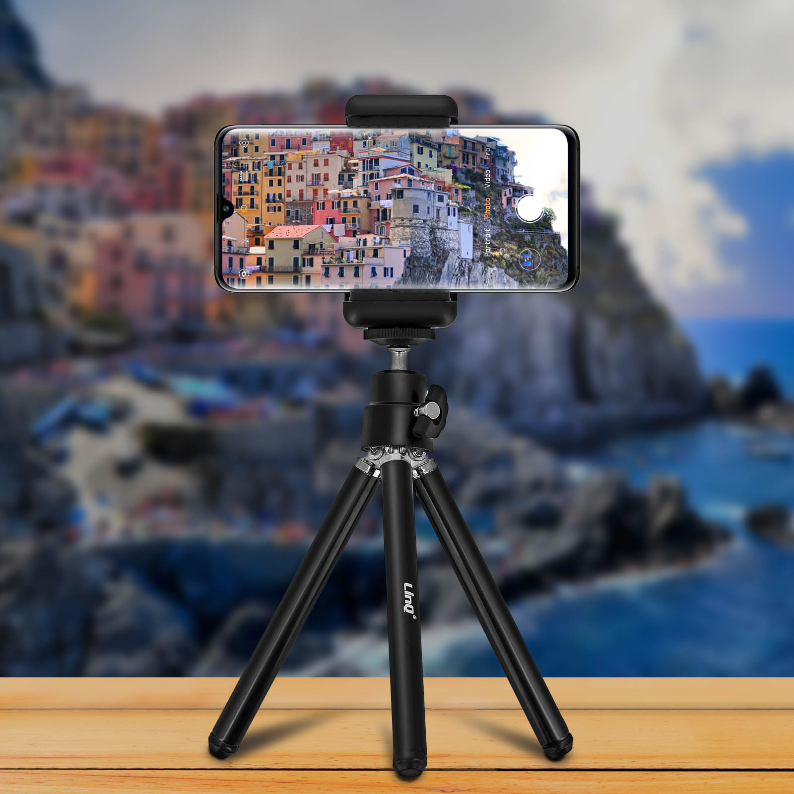 Un smartphone en un trípode que muestra una escena de un pueblo costero con el mar al fondo.