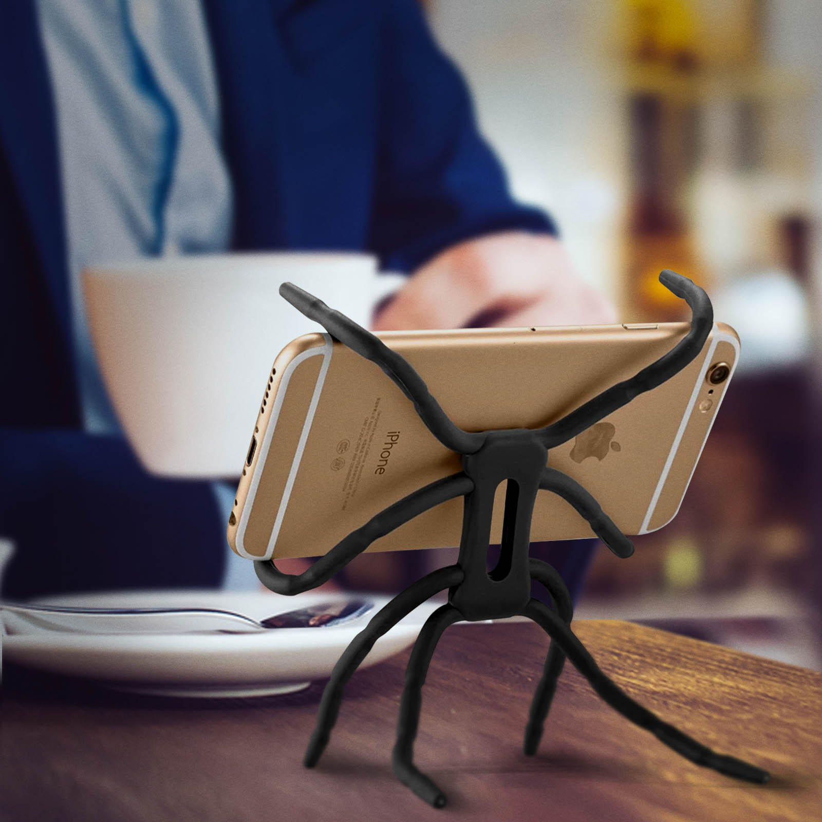 Un telefono è tenuto da un supporto per telefono nero flessibile. Una tazza e un piatto su un tavolo.
