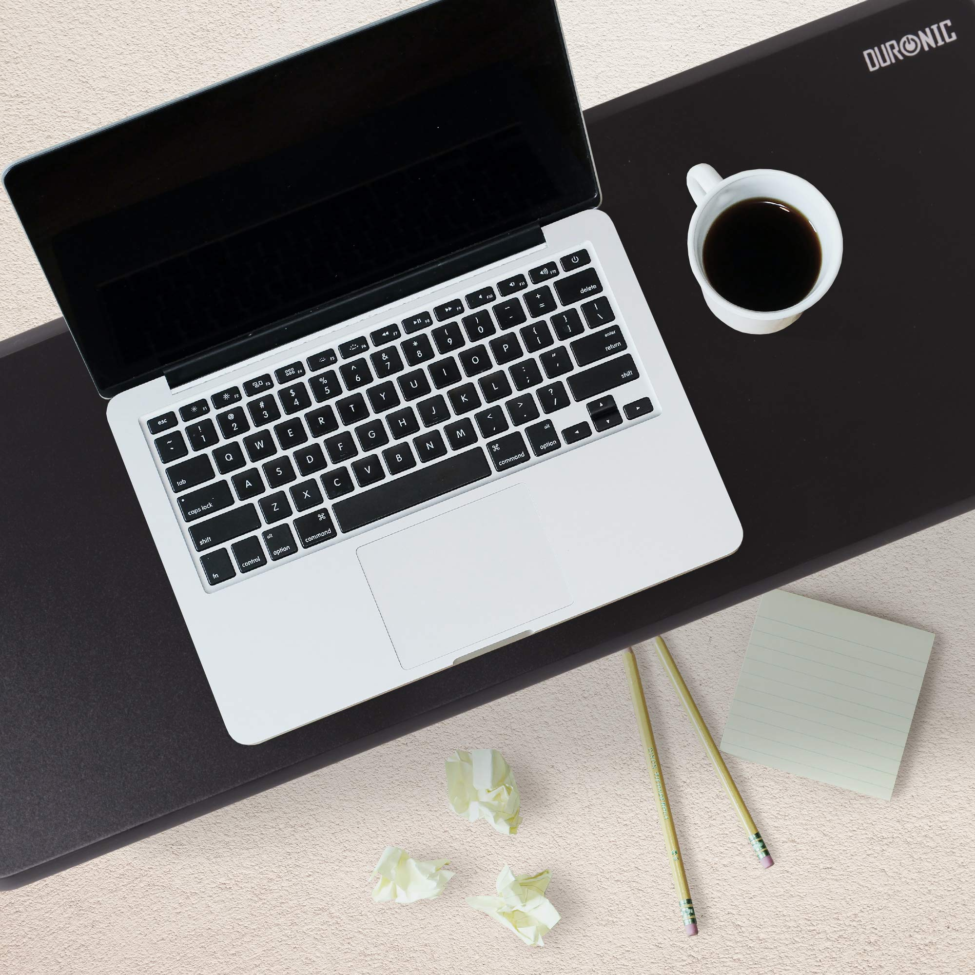 Laptop, Kaffeetasse, Bleistifte, zerknittertes Papier und Notizblock auf einem schwarzen Schreibtischpad.